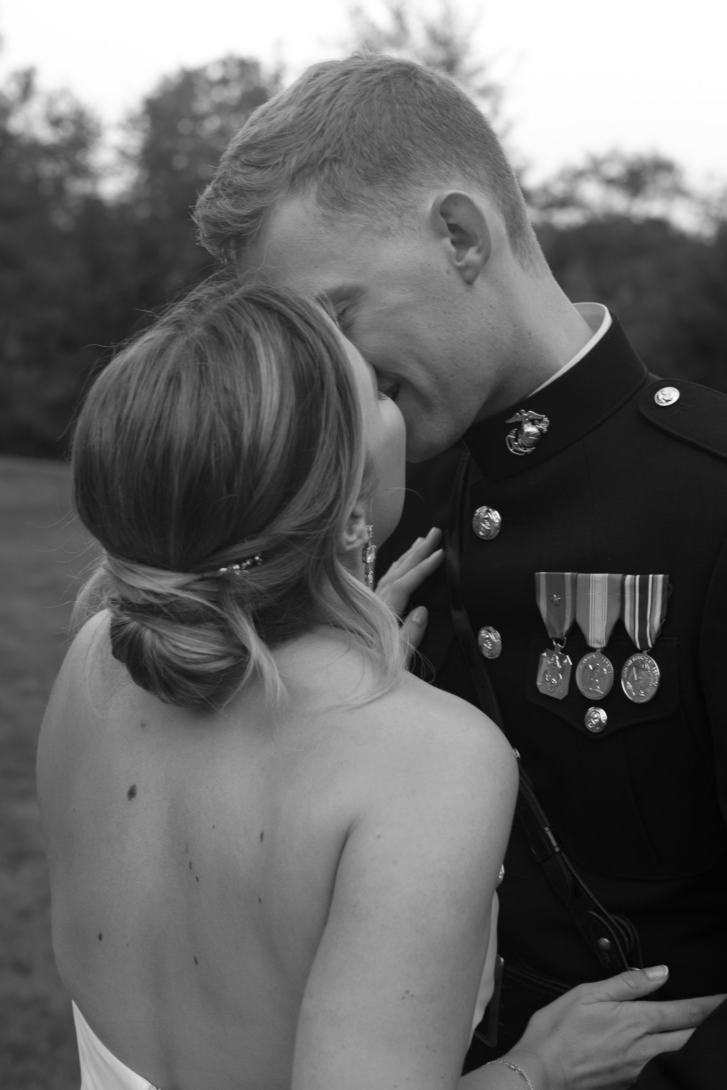Black and white intimate moment of a bride and Marine groom embracing forehead to forehead outdoors.