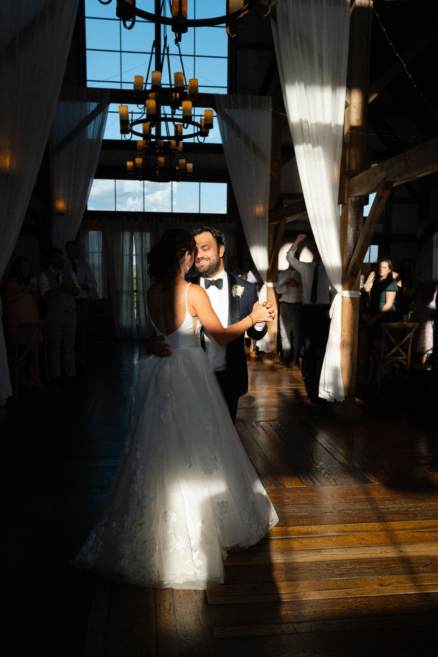 Newlyweds share an intimate first dance bathed in golden sunlight in a rustic barn wedding venue.