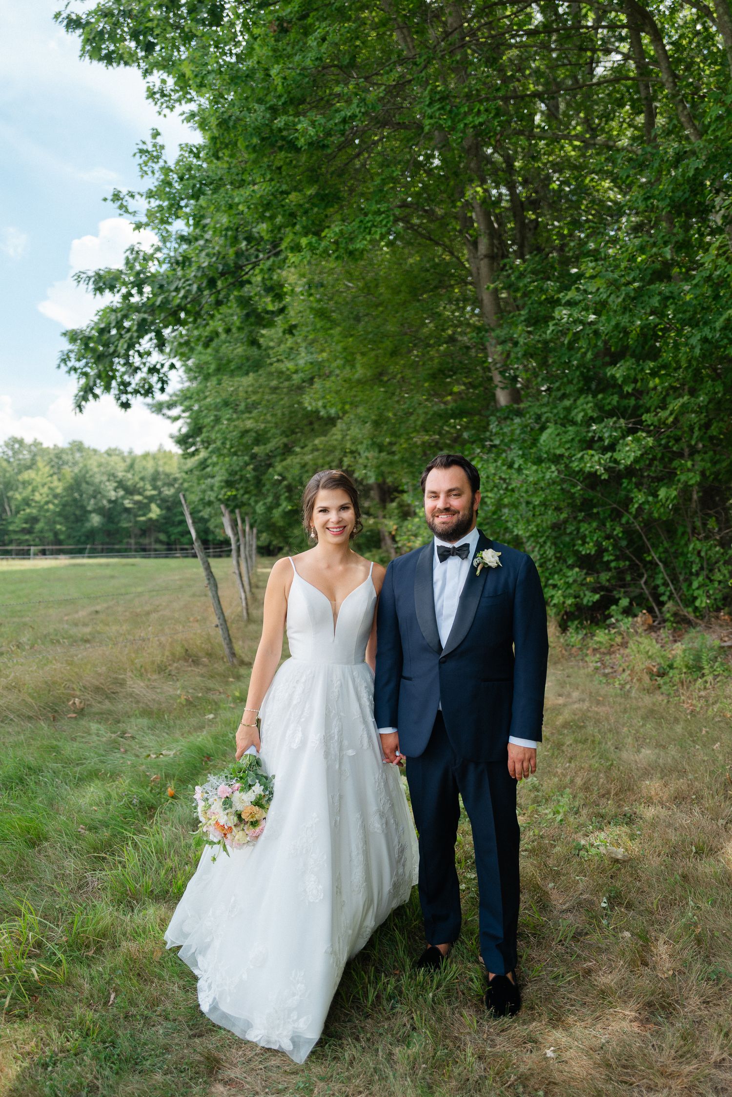 Bride and groom holding hands in a lush green outdoor setting, bride in a V-neck ball gown holding a bouquet.
