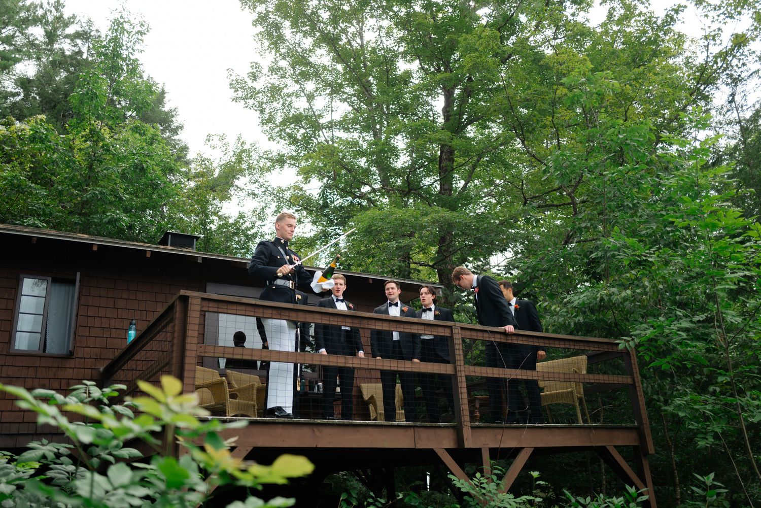 Groomsmen gathered on wooden deck surrounded by trees.