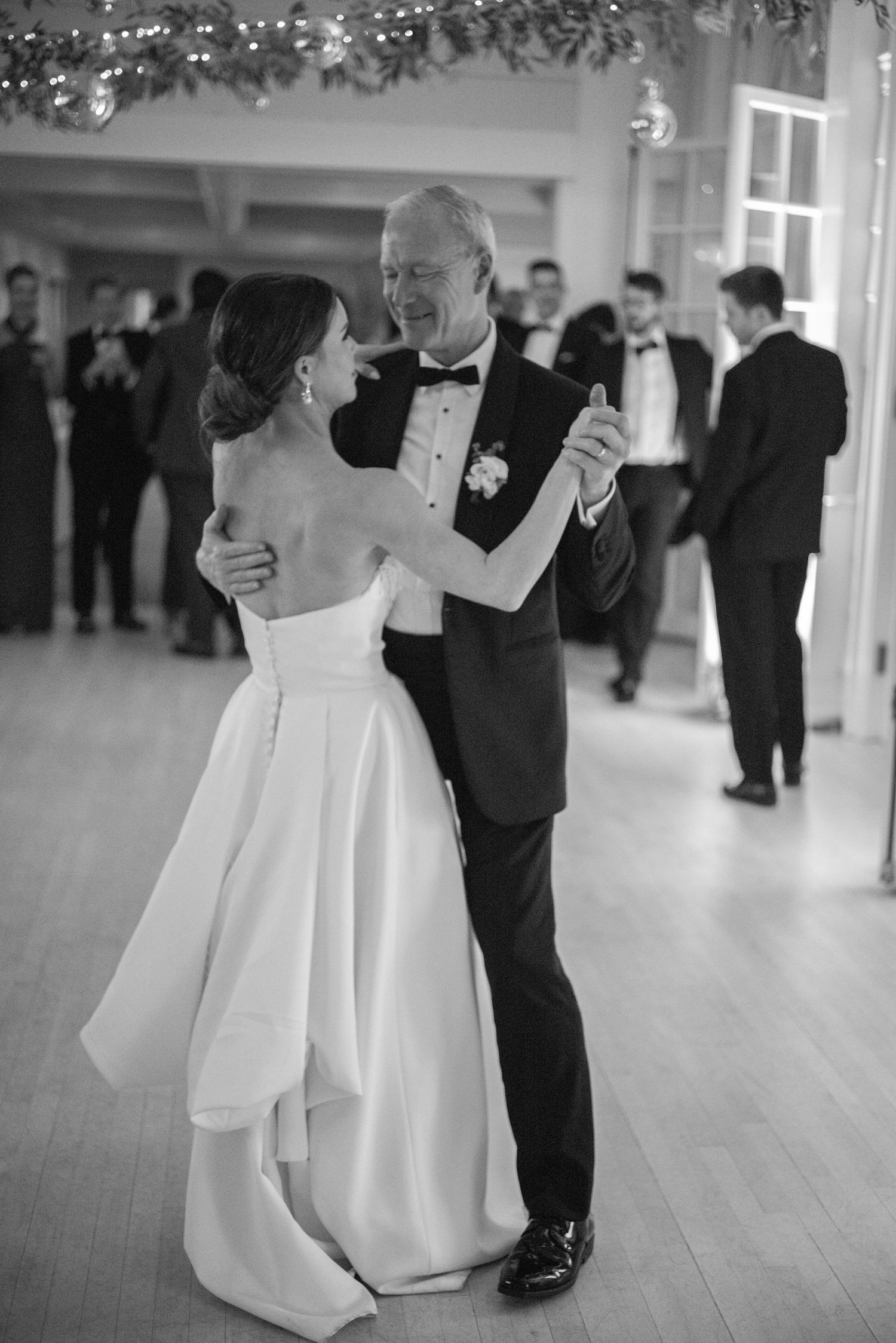 Black and white photo of bride in strapless gown sharing father-daughter dance at elegant wedding.