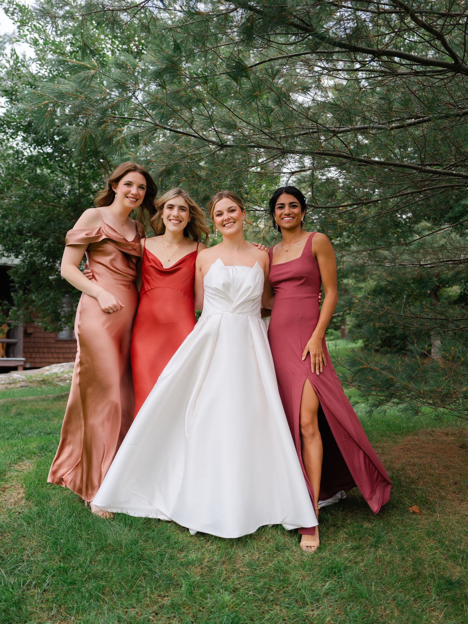 Bride with three bridesmaids in colorful gowns outdoors.