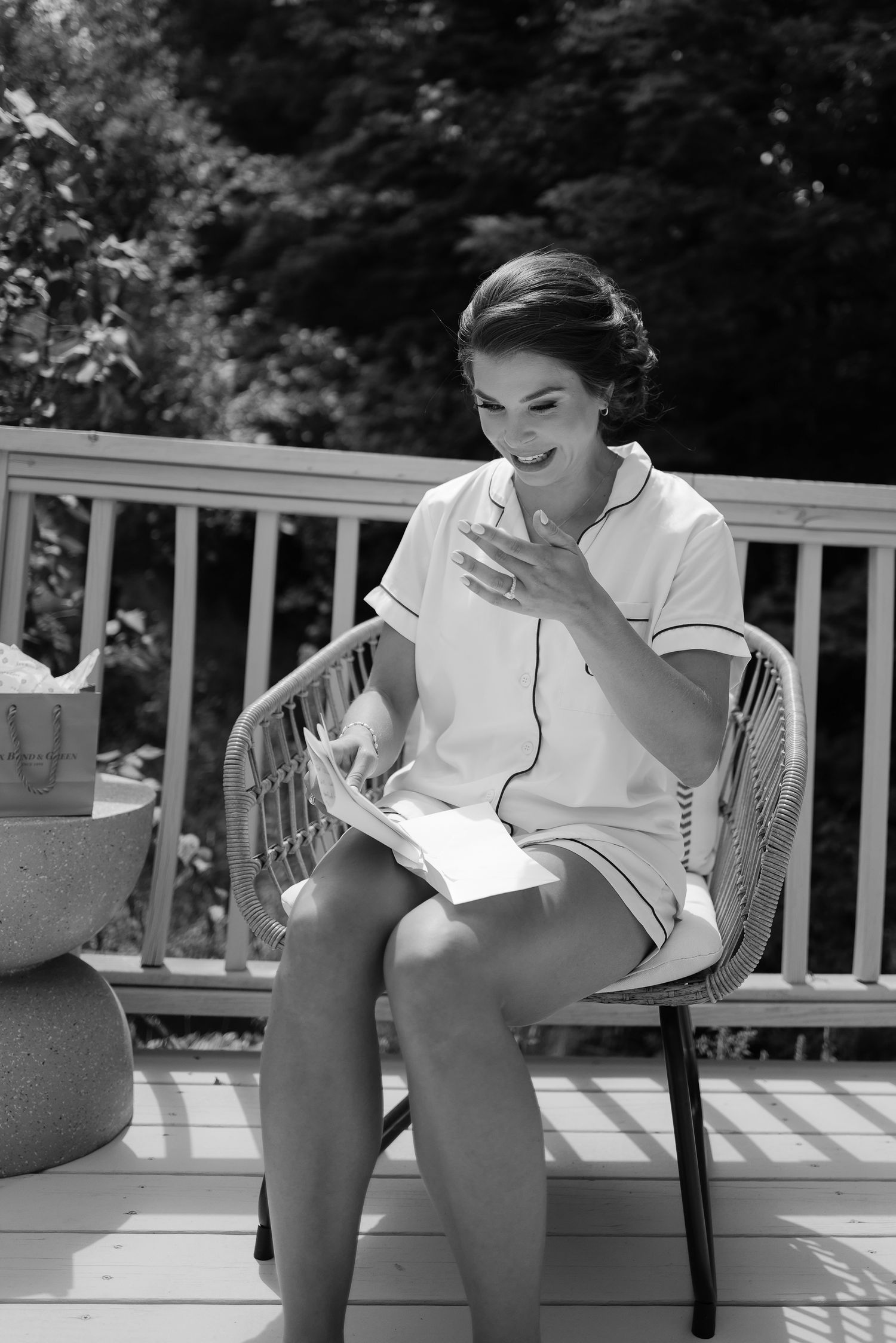Black and white photo of bride in white robe reading letter on deck.