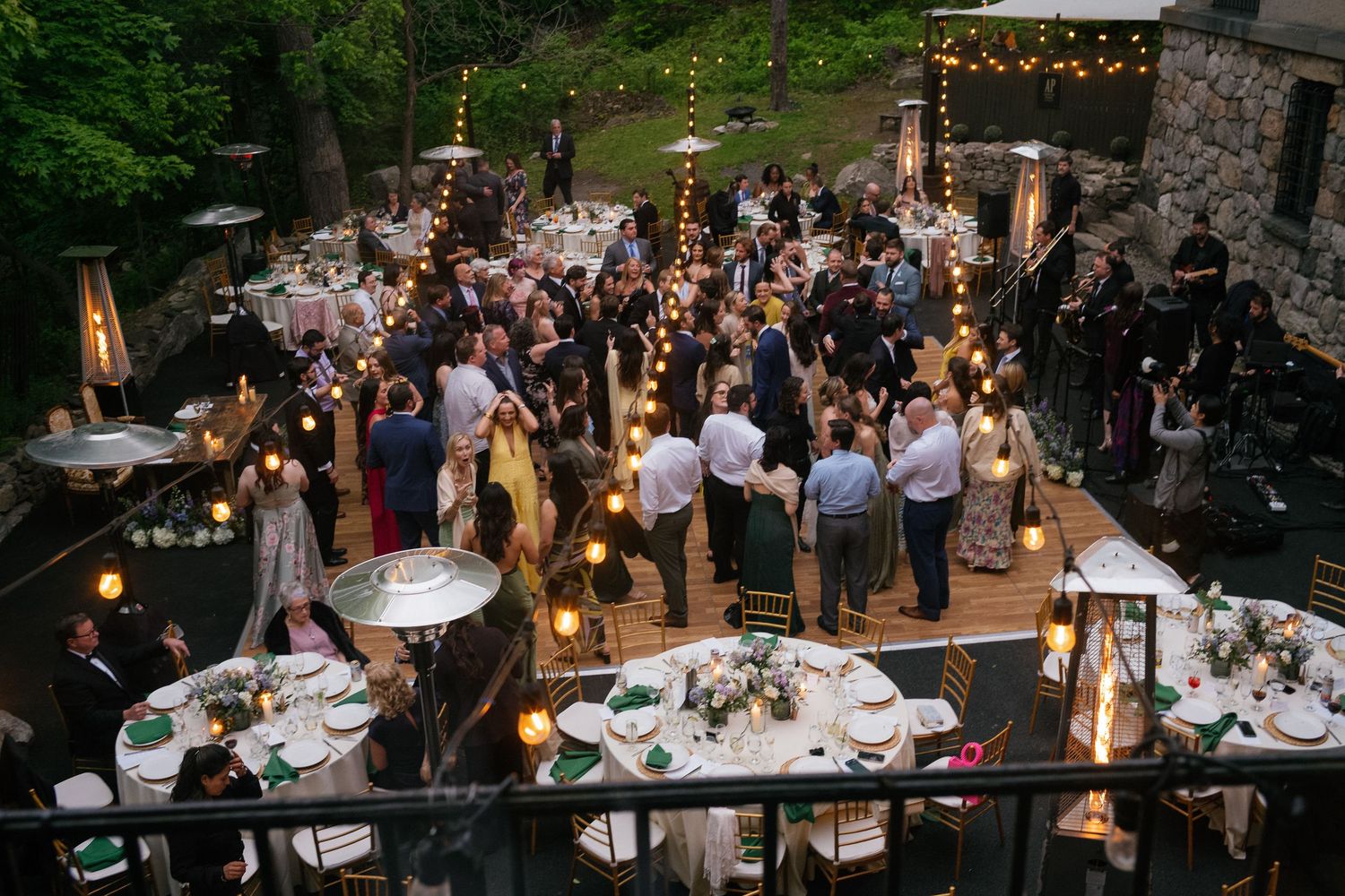 Aerial view of guests mingling at an elegant outdoor evening wedding reception with warm string lighting.