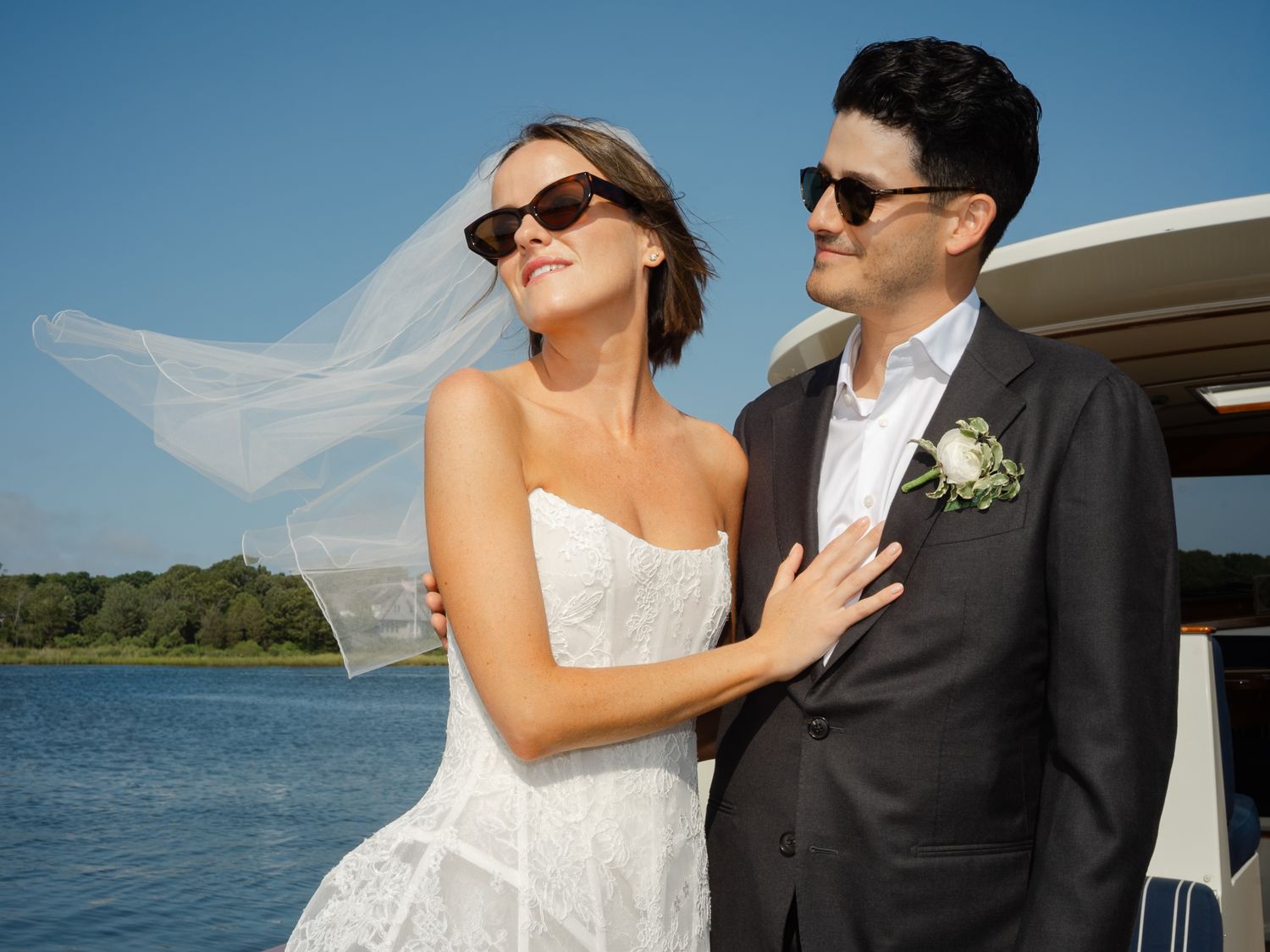 Bride in white dress and veil with groom in gray suit posing on a boat on a sunny wedding day.