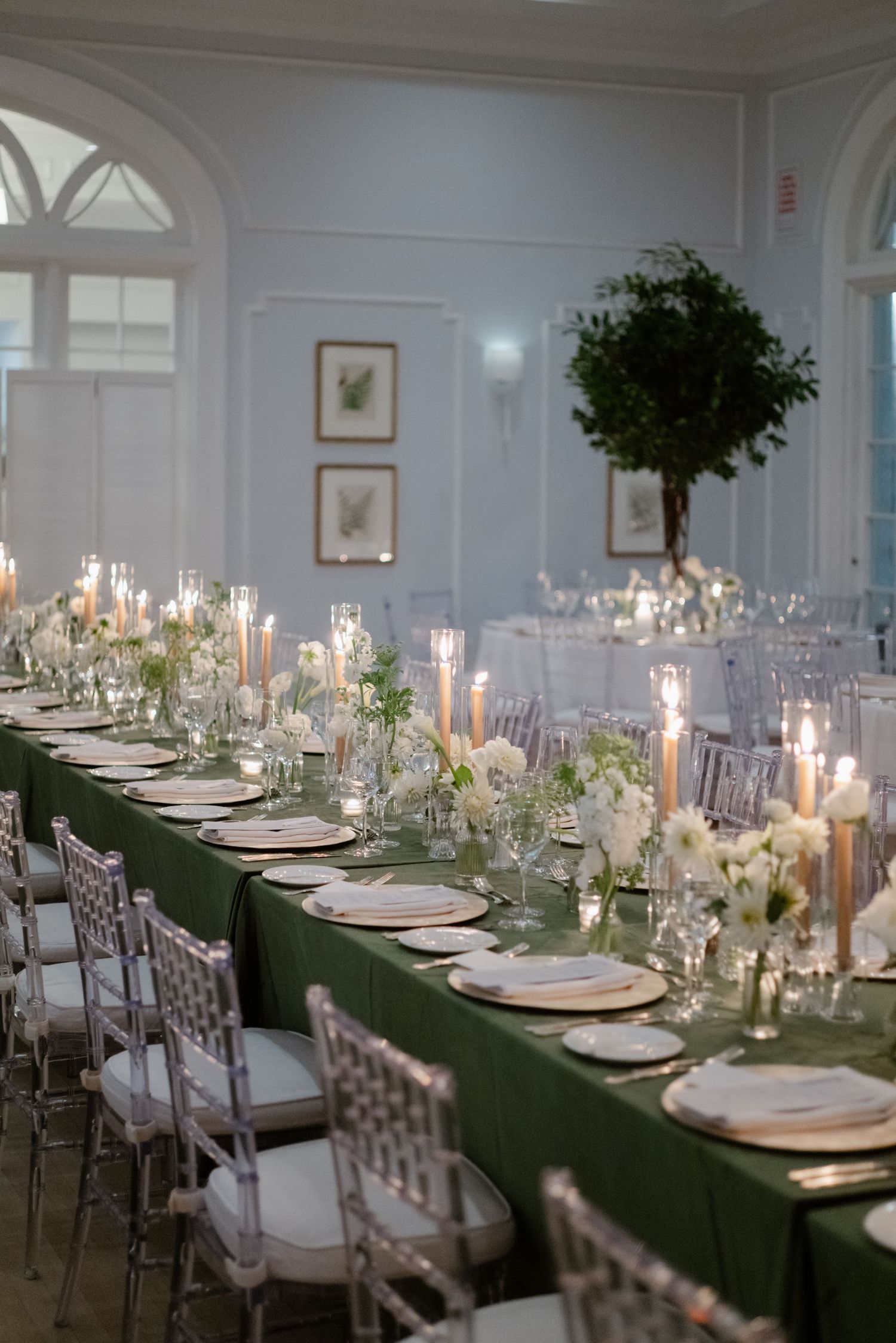 Elegant wedding reception with long green linen tables, white floral centerpieces, and candlelight.