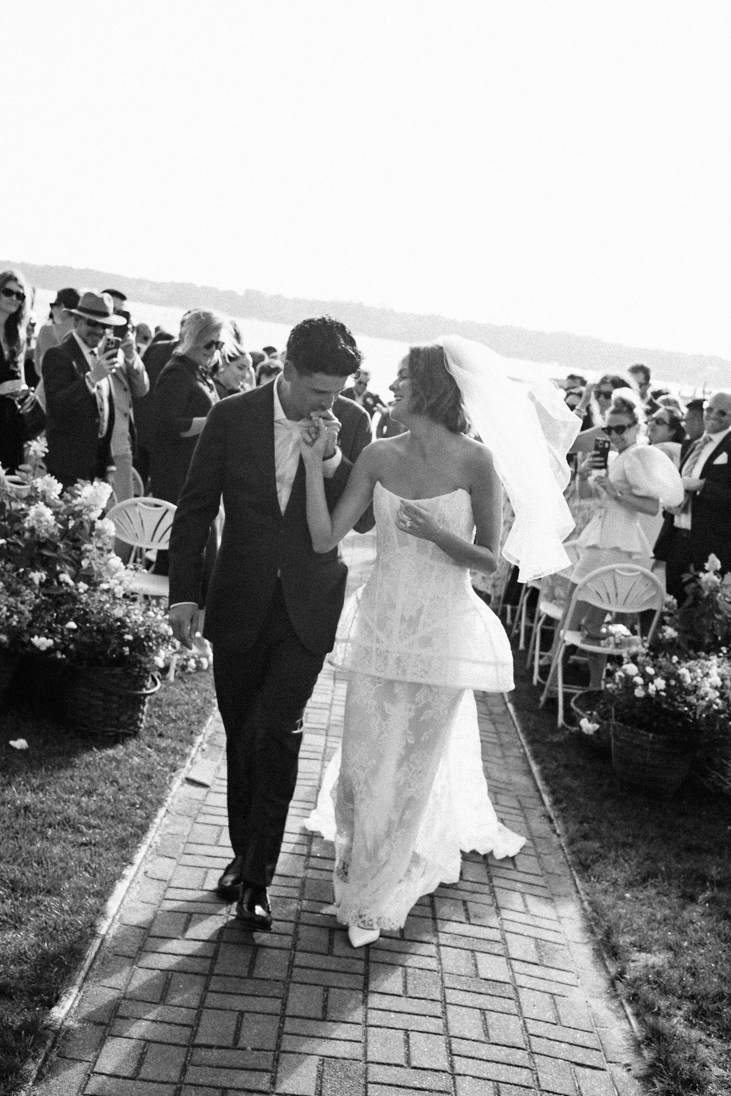 Black and white photo of a bride and groom walking down the aisle after their outdoor waterfront wedding ceremony.