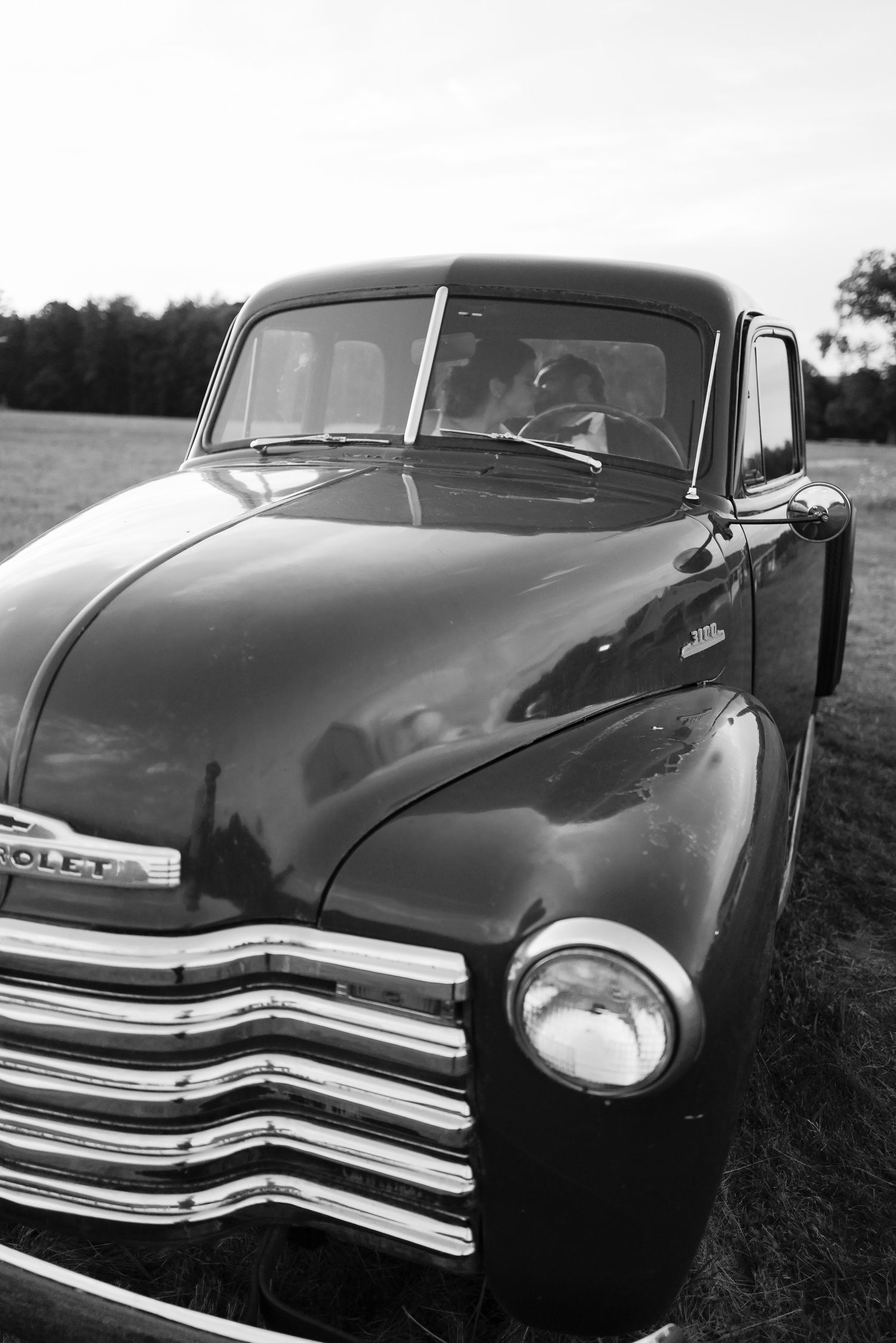 Vintage Chevrolet truck photographed in black and white at a rustic outdoor wedding venue.