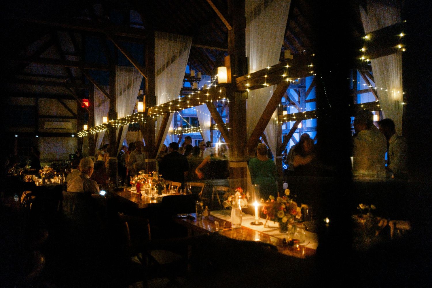 Warmly lit rustic barn wedding reception with candles, string lights, and elegant decor.