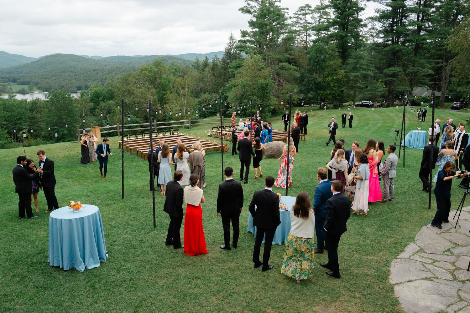 Outdoor wedding cocktail hour on a scenic lawn with mountain views, guests mingling around tables.