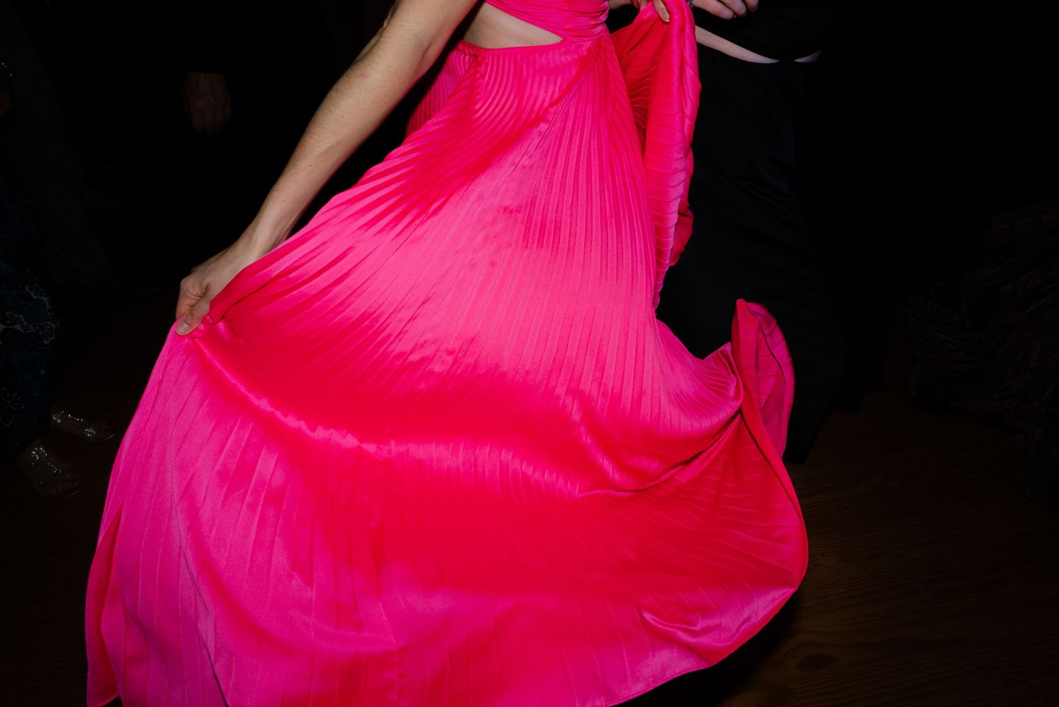 A woman twirls in a vibrant hot pink pleated ballgown, capturing the flowing movement of the fabric.