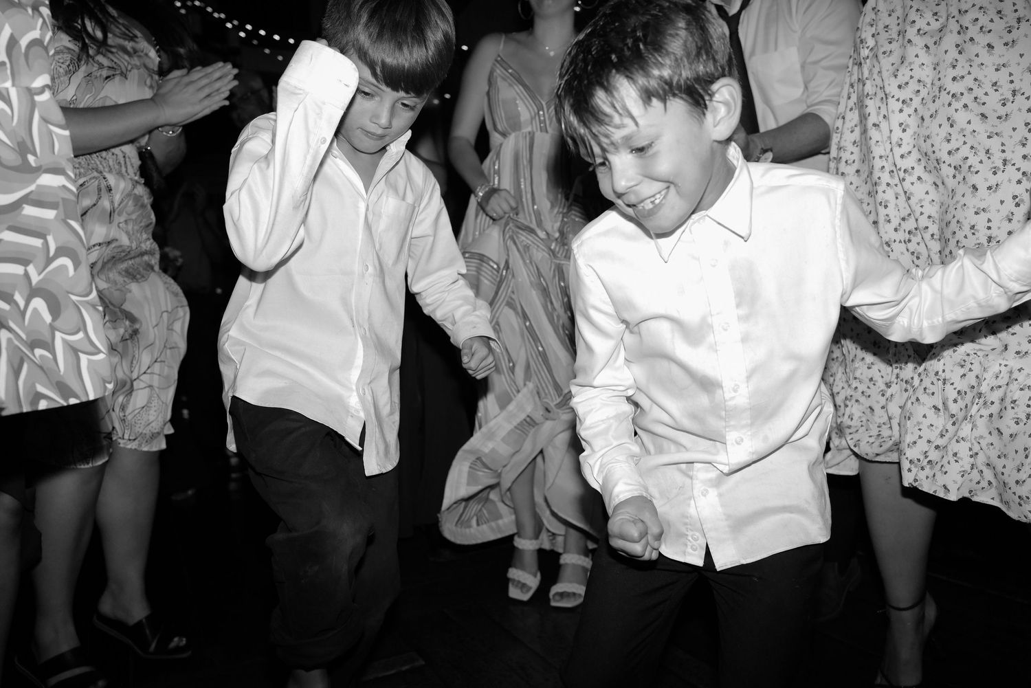 Two young boys dancing energetically in black and white photo at a wedding reception.