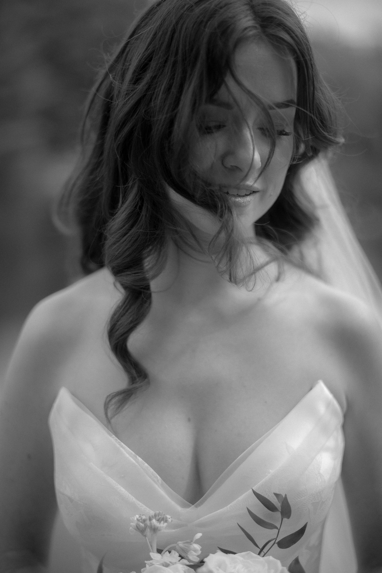Bride in strapless floral wedding gown looks down holding bouquet in black and white portrait.