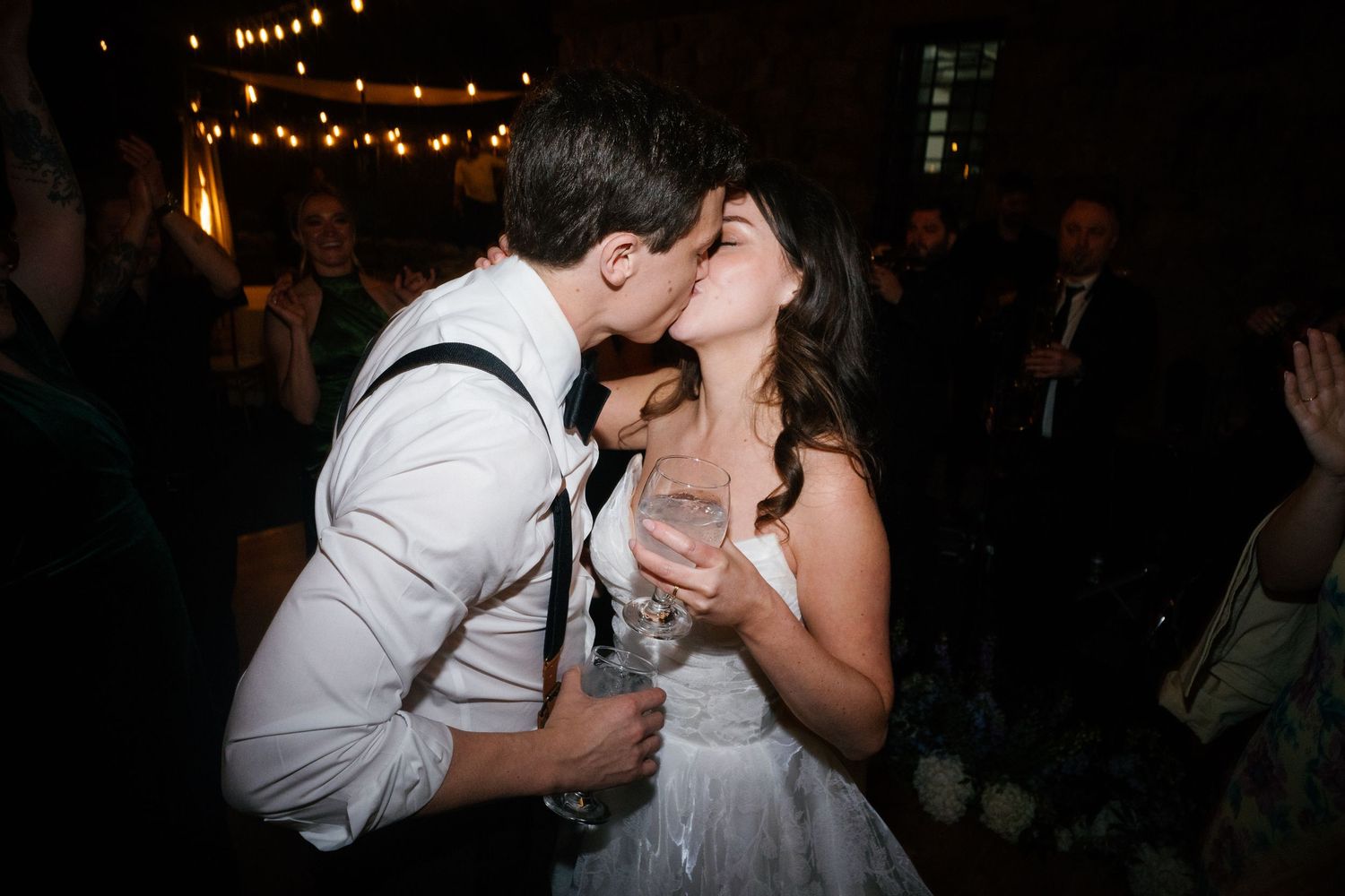 Bride and groom share romantic kiss while holding champagne glasses at wedding reception.