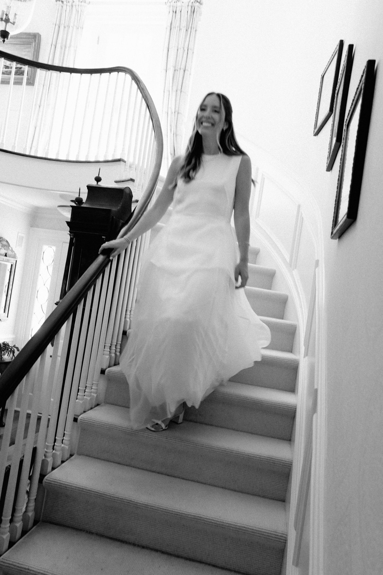 Radiant bride in flowing white wedding gown descends grand staircase with curved banister.