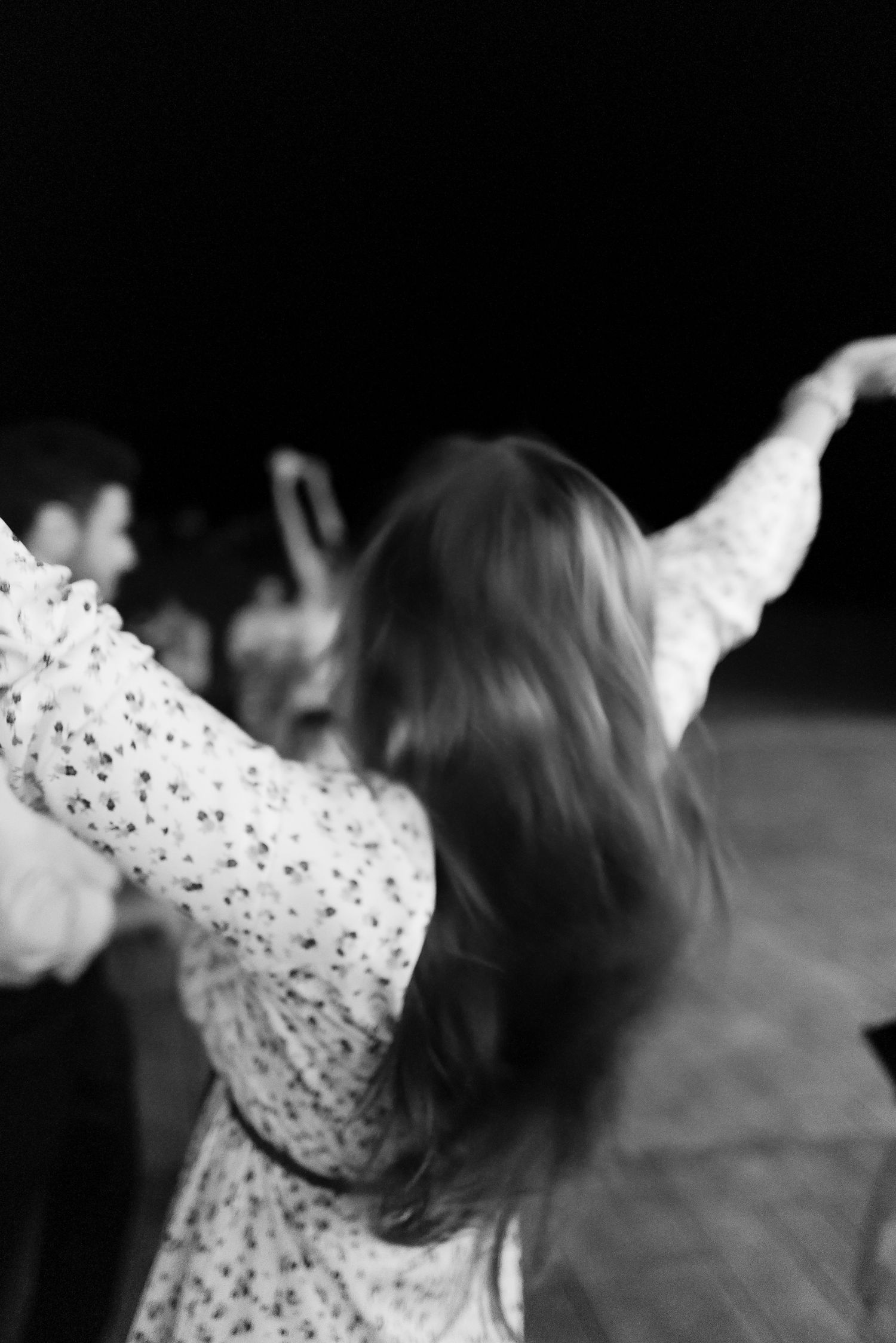 Woman in floral dress dancing with arms outstretched at lively wedding reception.