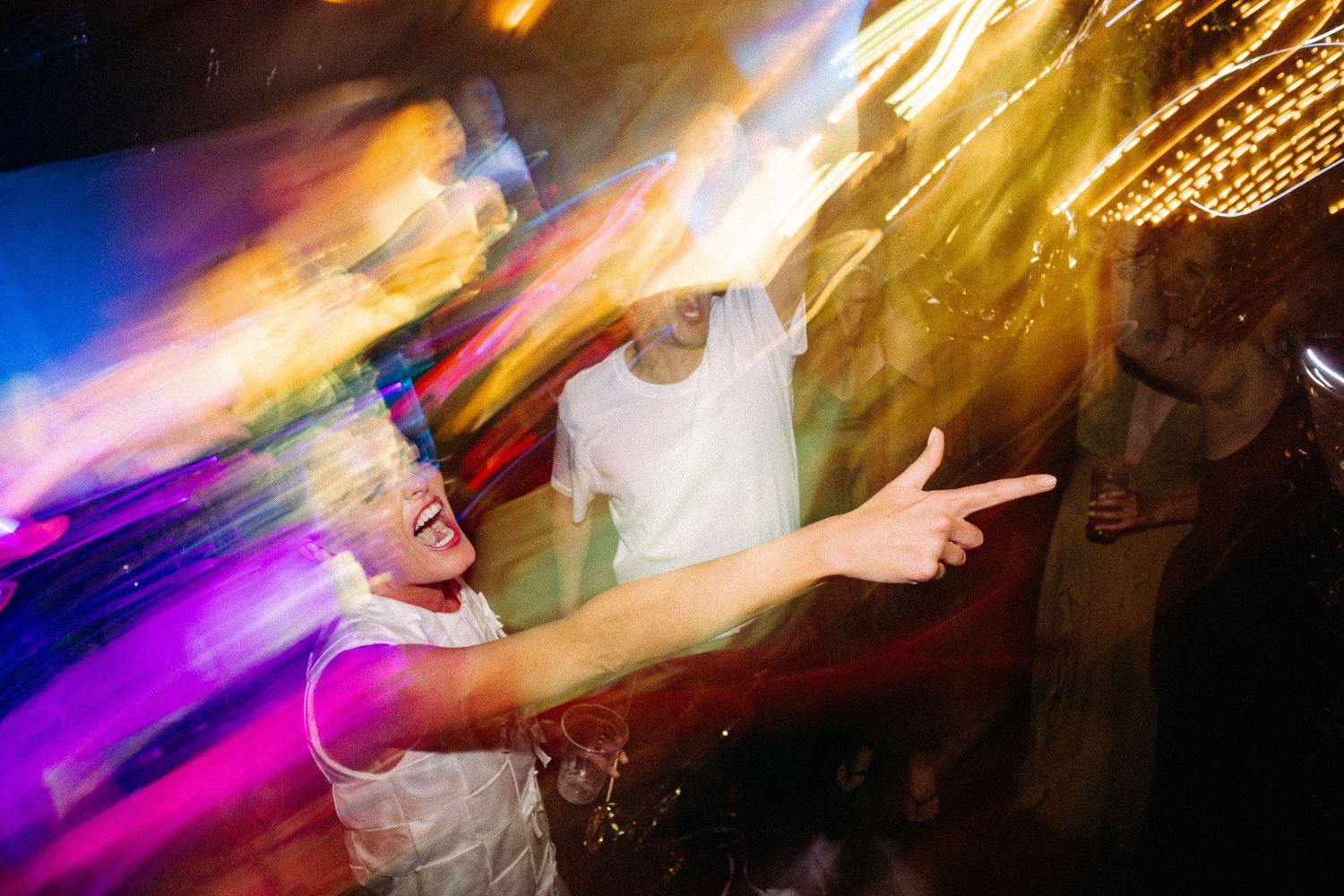 People dancing at a nightclub with colorful light trails and motion blur effects.