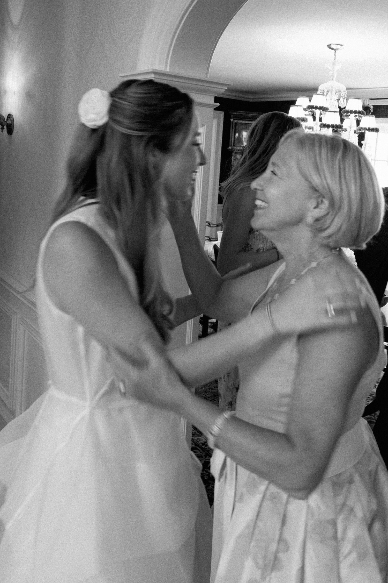 Bride and mother share emotional embrace while laughing together during wedding morning preparations.