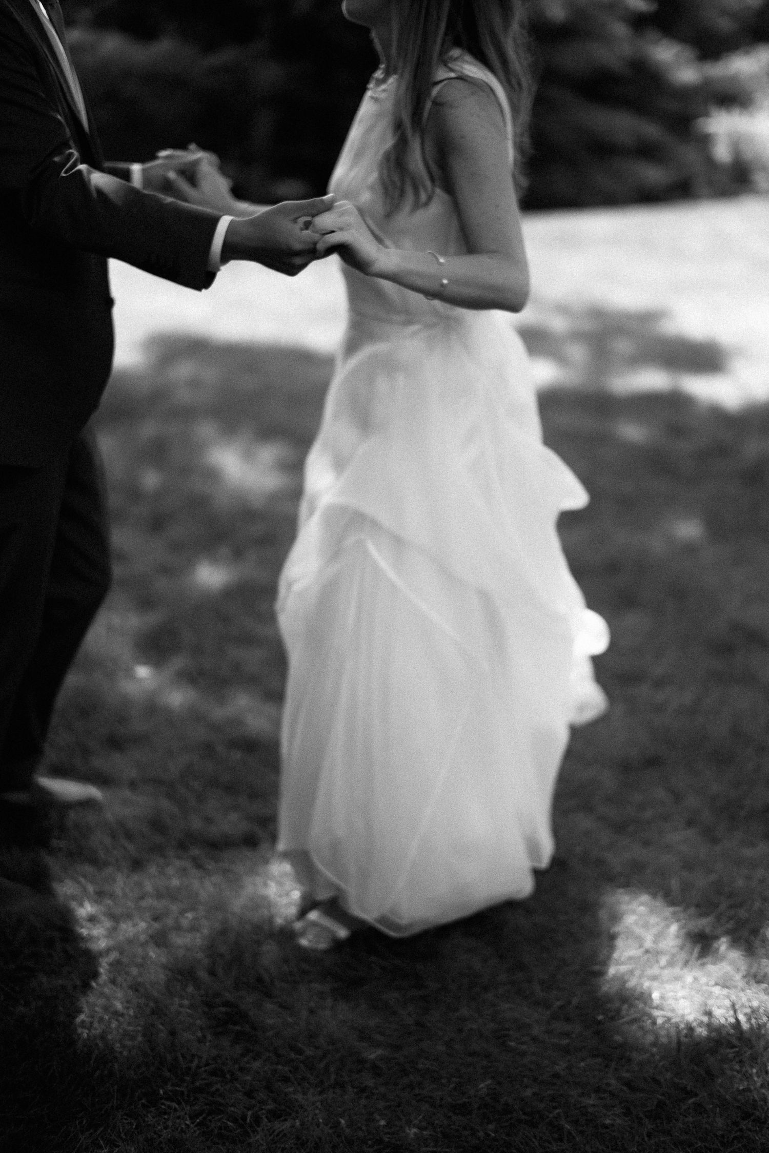 Black and white photo of bride and groom holding hands outdoors during wedding ceremony.