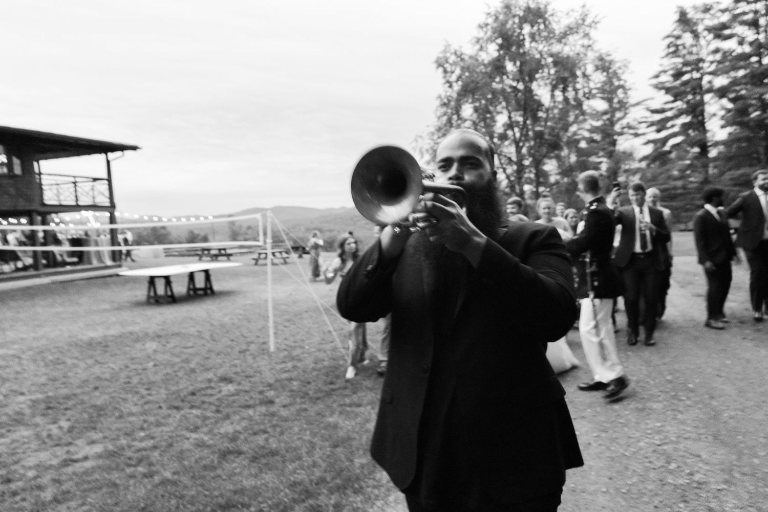 Black and white photo of a musician playing trumpet outdoors during a wedding celebration.
