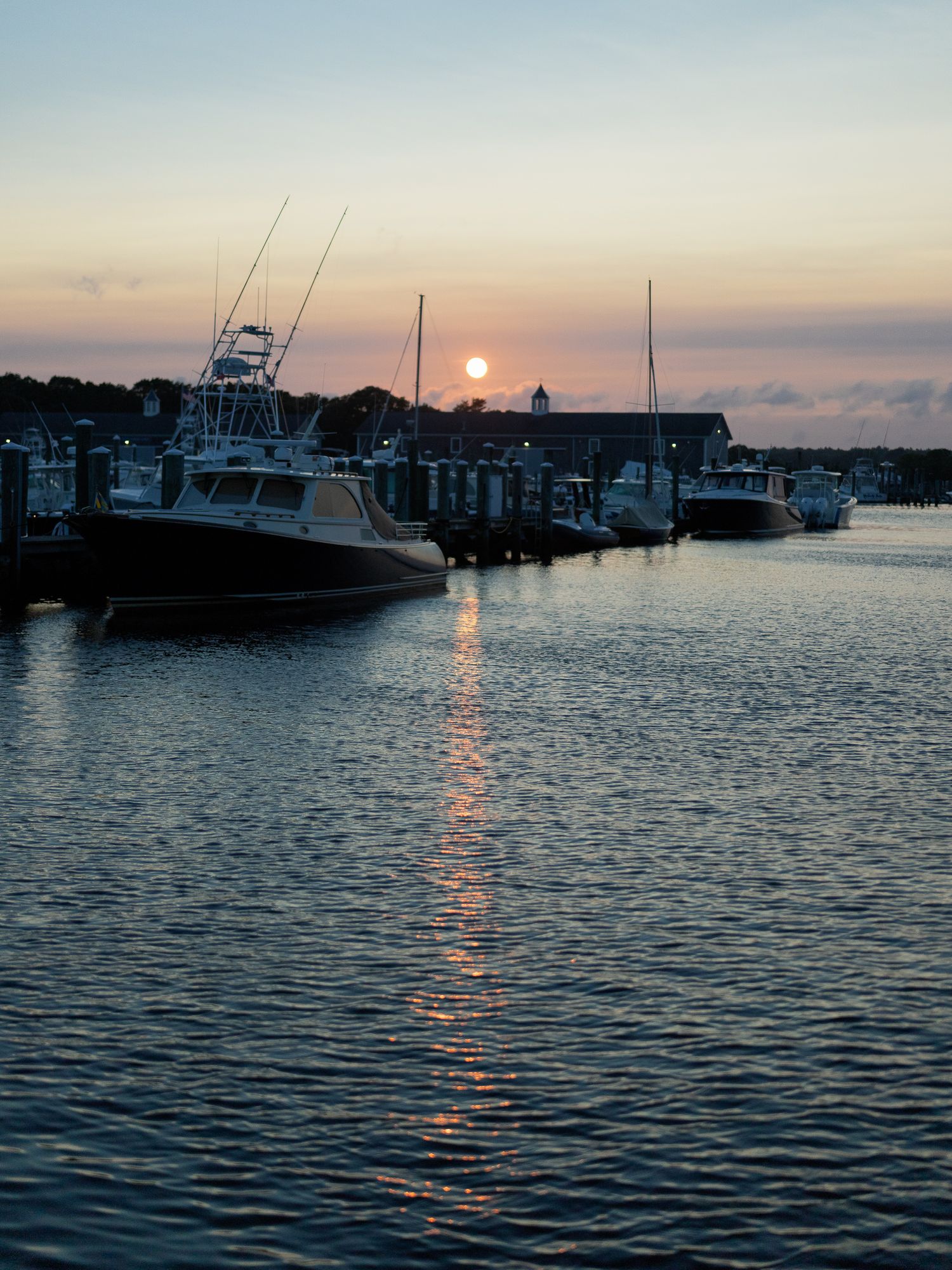 Boats moored at a peaceful marina dock reflecting golden sunset light on calm water.