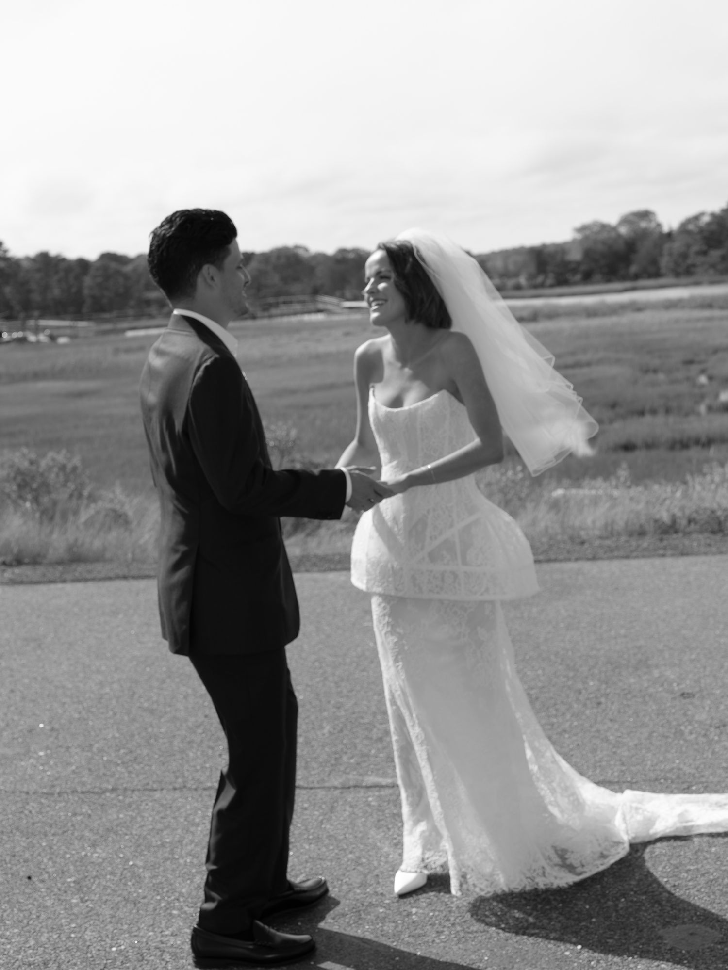 Black and white photo of bride and groom holding hands outdoors on their wedding day.
