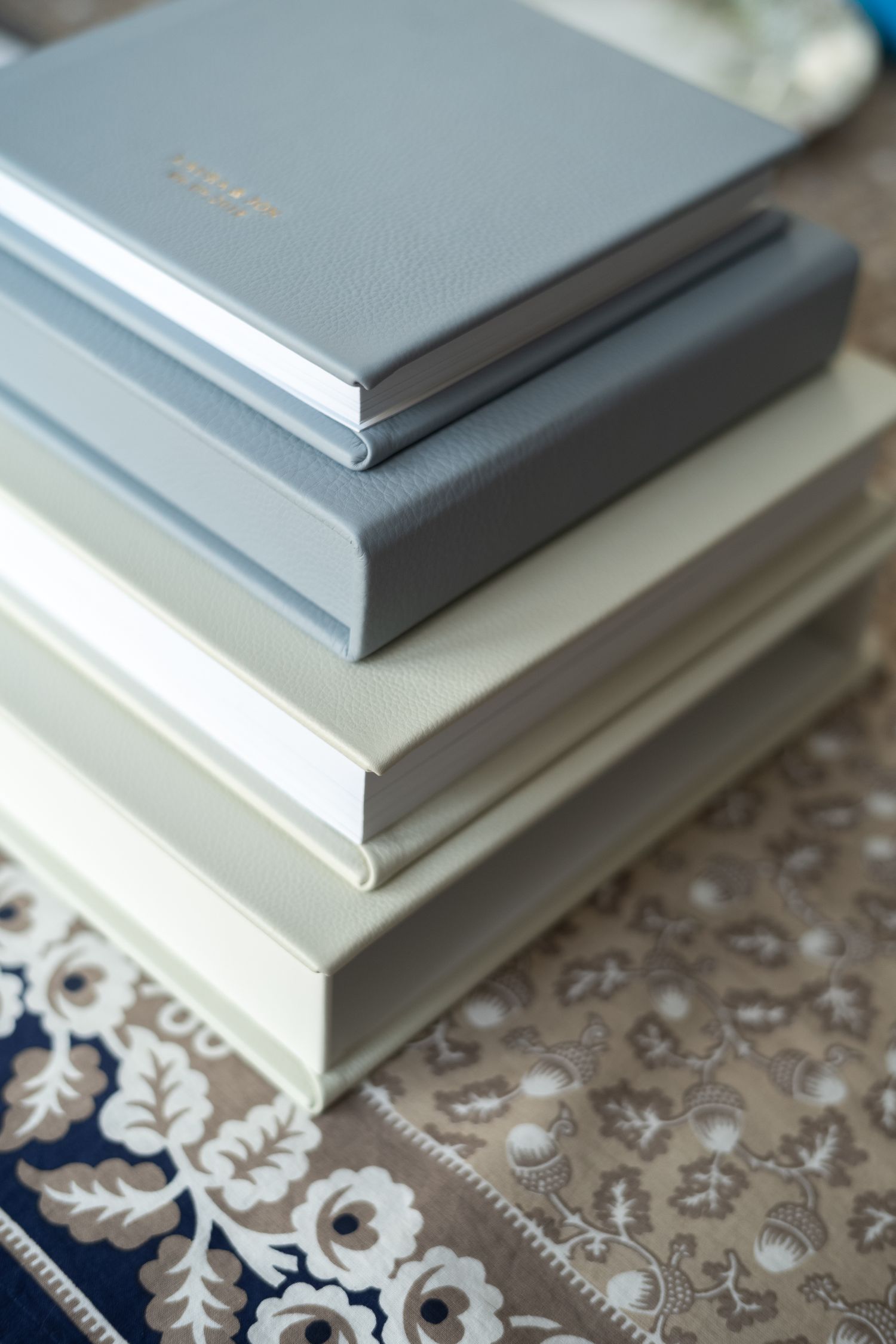 Stack of four elegant hardcover wedding photo albums in gray and cream tones on floral surface.