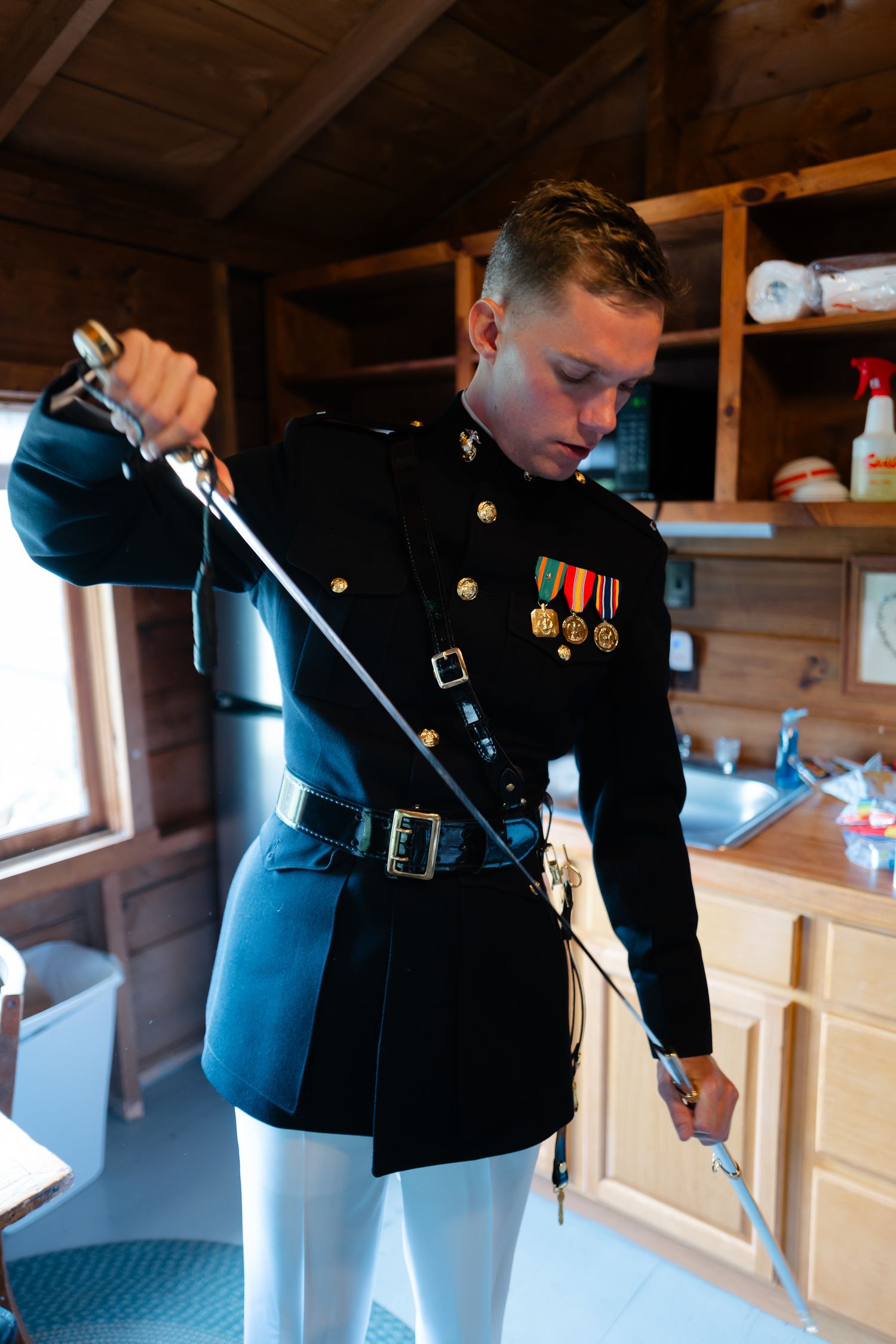 Marine in dress blues uniform inspecting sword indoors.