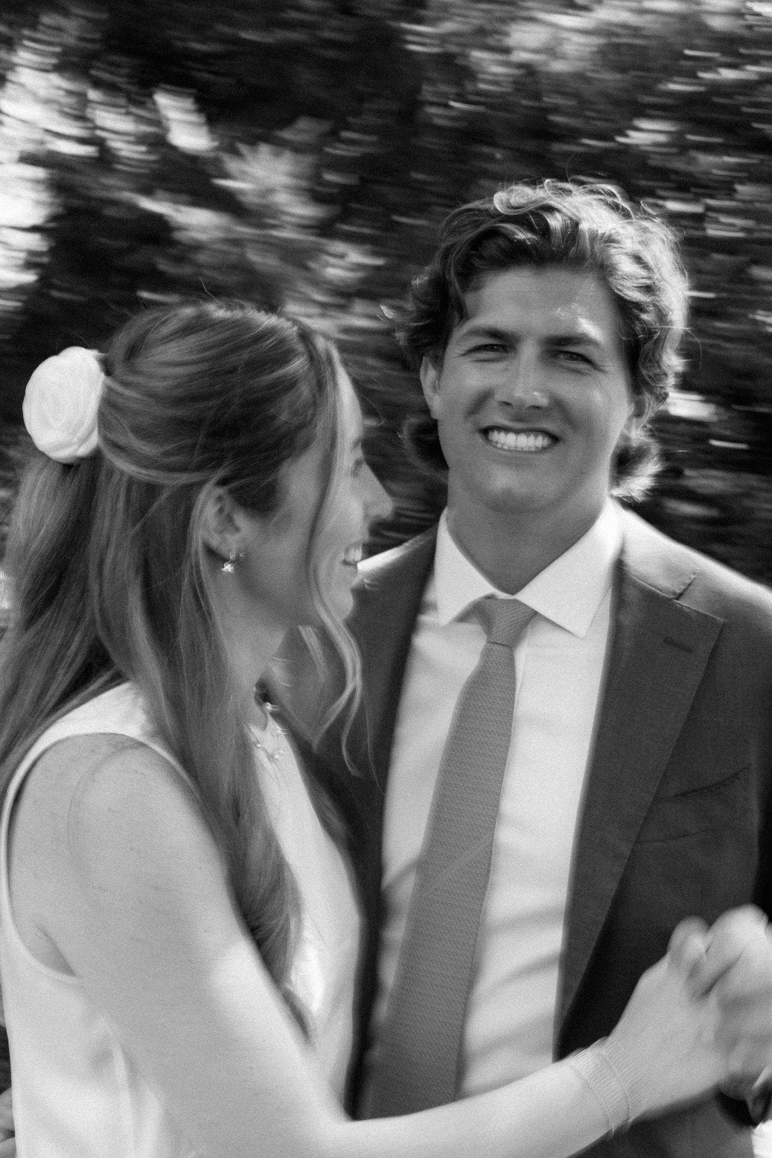 Smiling bride and groom dancing together in black and white wedding portrait outdoors.