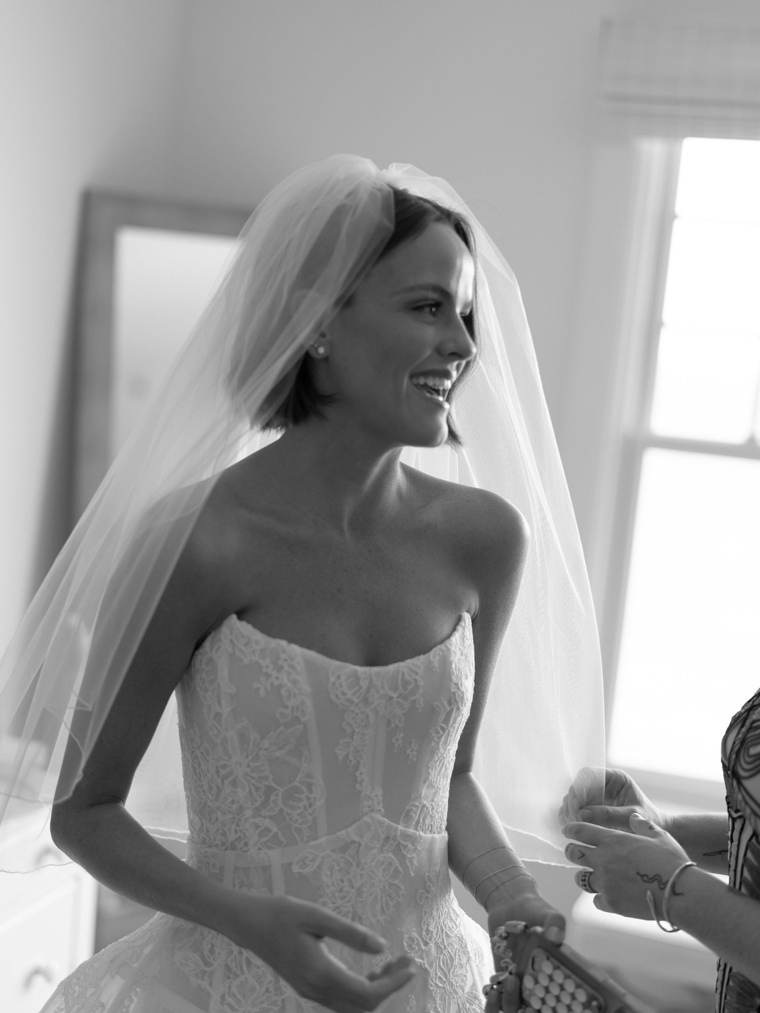 Smiling bride in strapless lace wedding dress and veil, black and white candid photo.