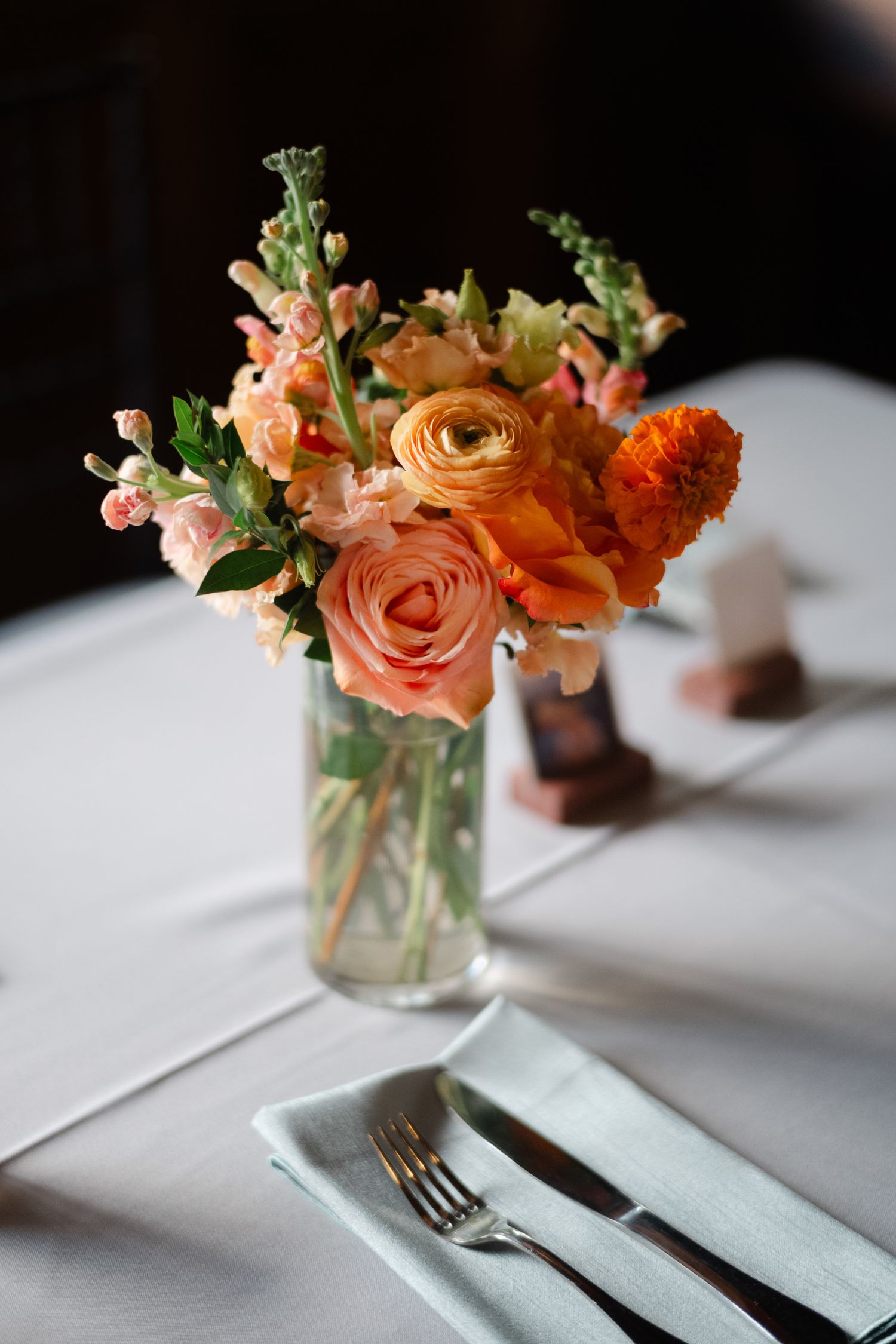 Elegant wedding table setting with peach and orange ranunculus floral centerpiece in a glass vase.