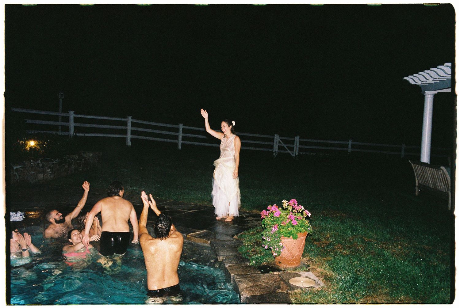Bride in white gown celebrating with guests in a pool during a late-night wedding after-party.