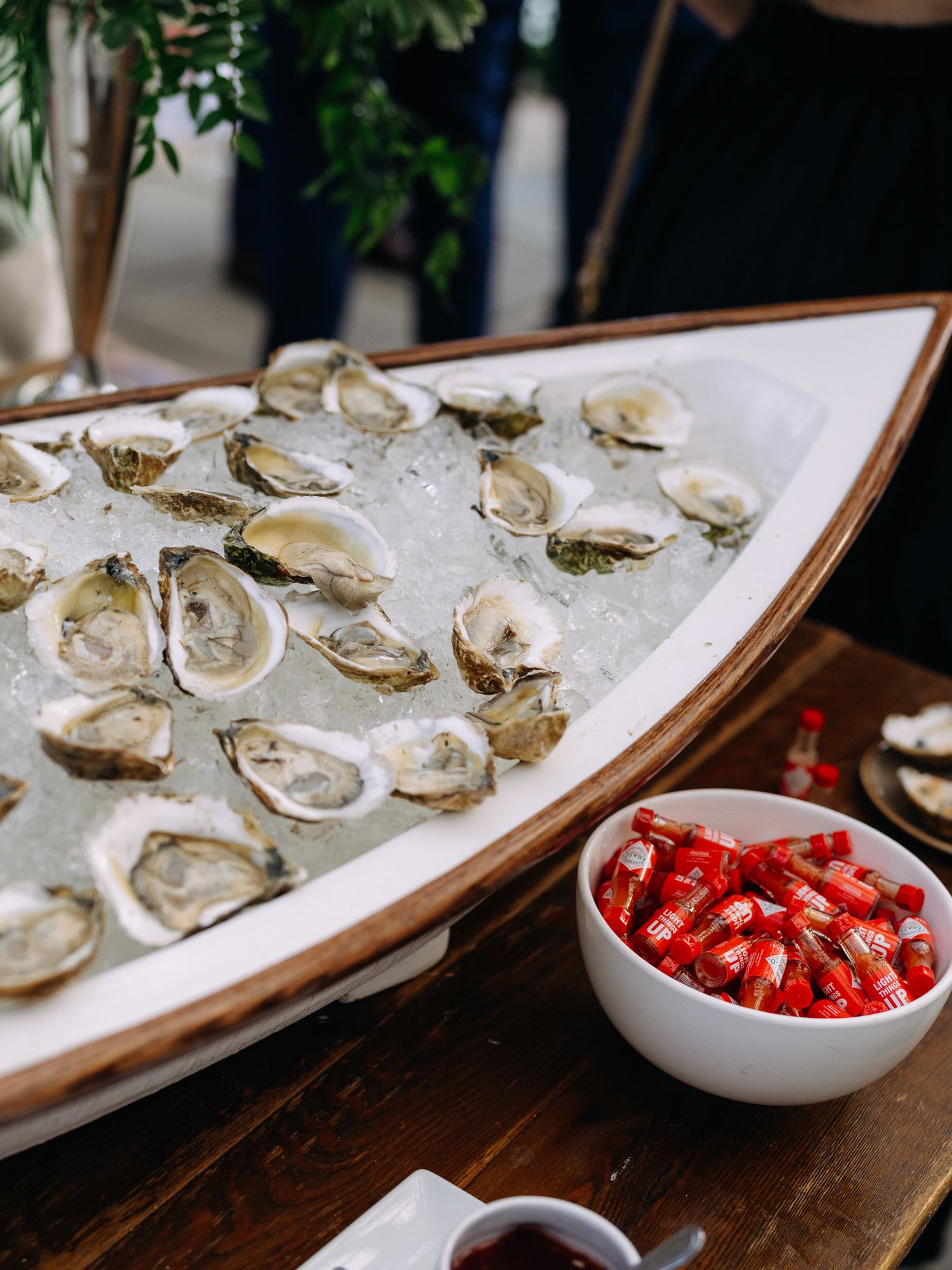 Fresh oysters on ice served in wooden boat-shaped display at wedding cocktail hour.