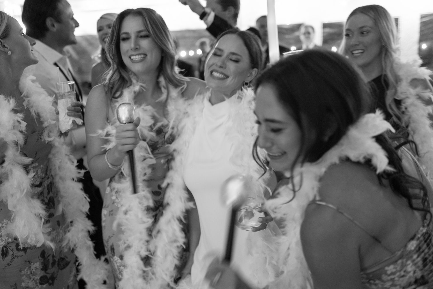 Bridesmaids wearing feather boas laughing and celebrating at wedding reception party.