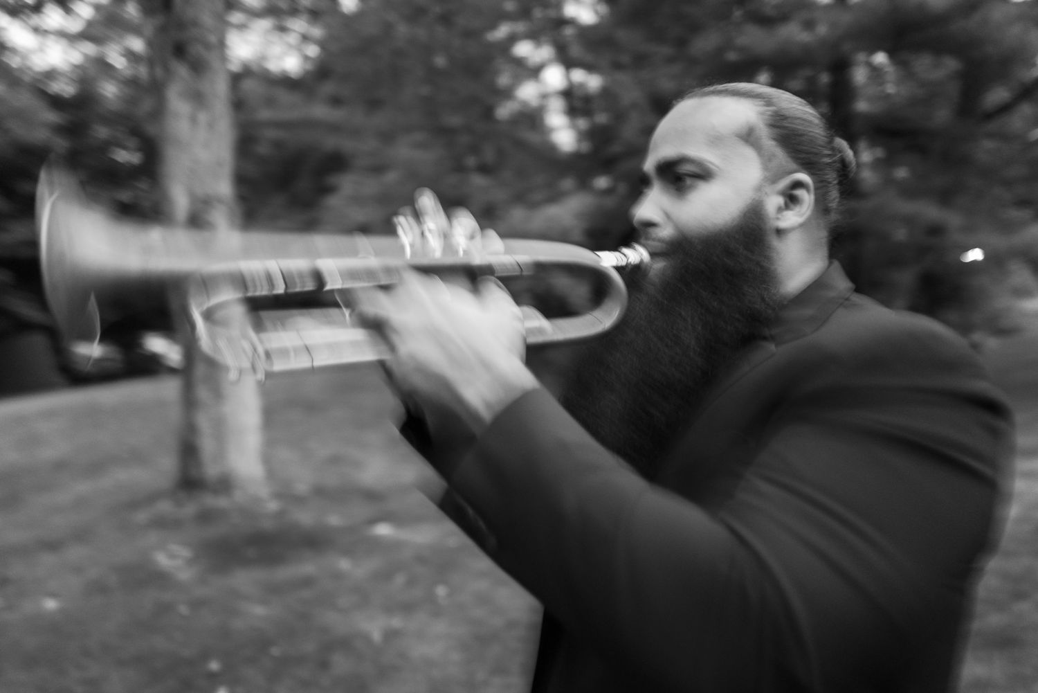 Bearded musician playing trumpet outdoors in black and white, captured with motion blur during a wedding celebration.
