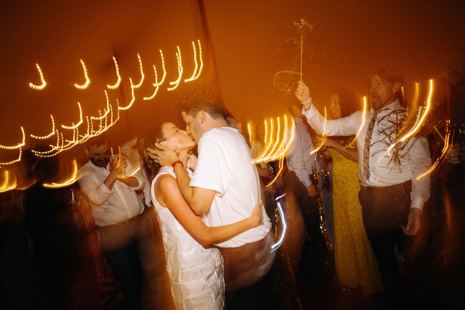 Couple sharing a romantic kiss on the dance floor surrounded by golden light trails at a wedding reception.