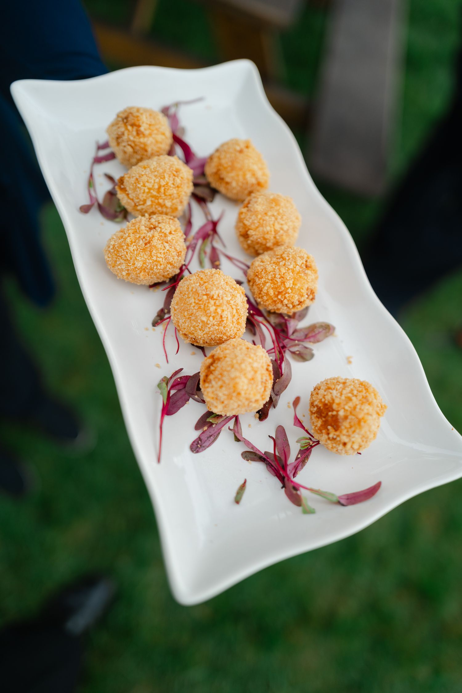Golden breaded appetizer balls served on a white rectangular plate with purple microgreens at a wedding reception.
