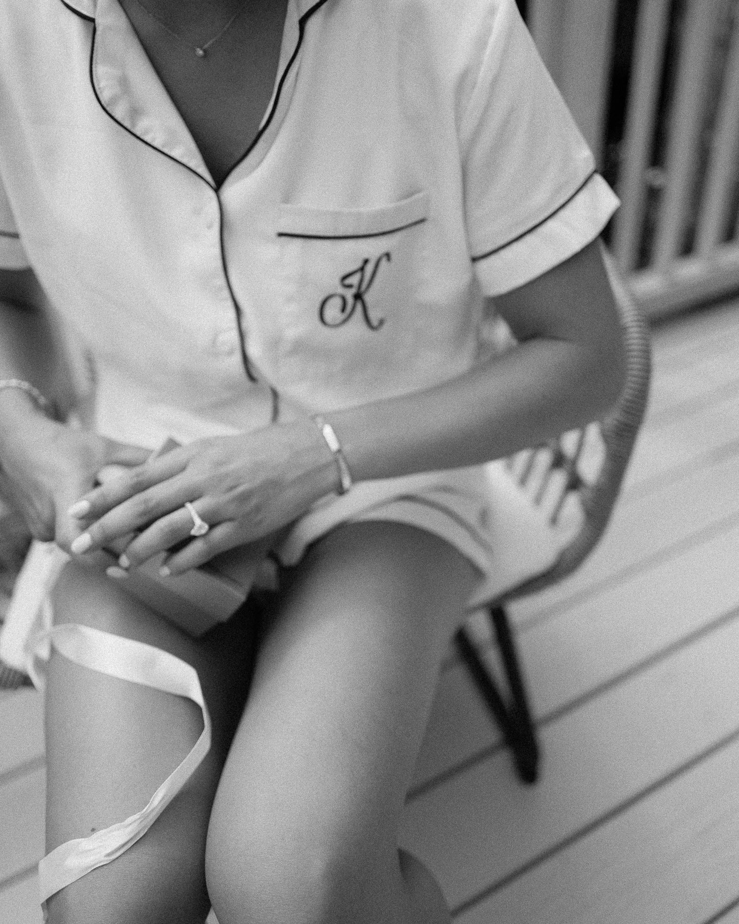 Bride in monogrammed white pajamas sitting in chair with wedding garter on her leg.