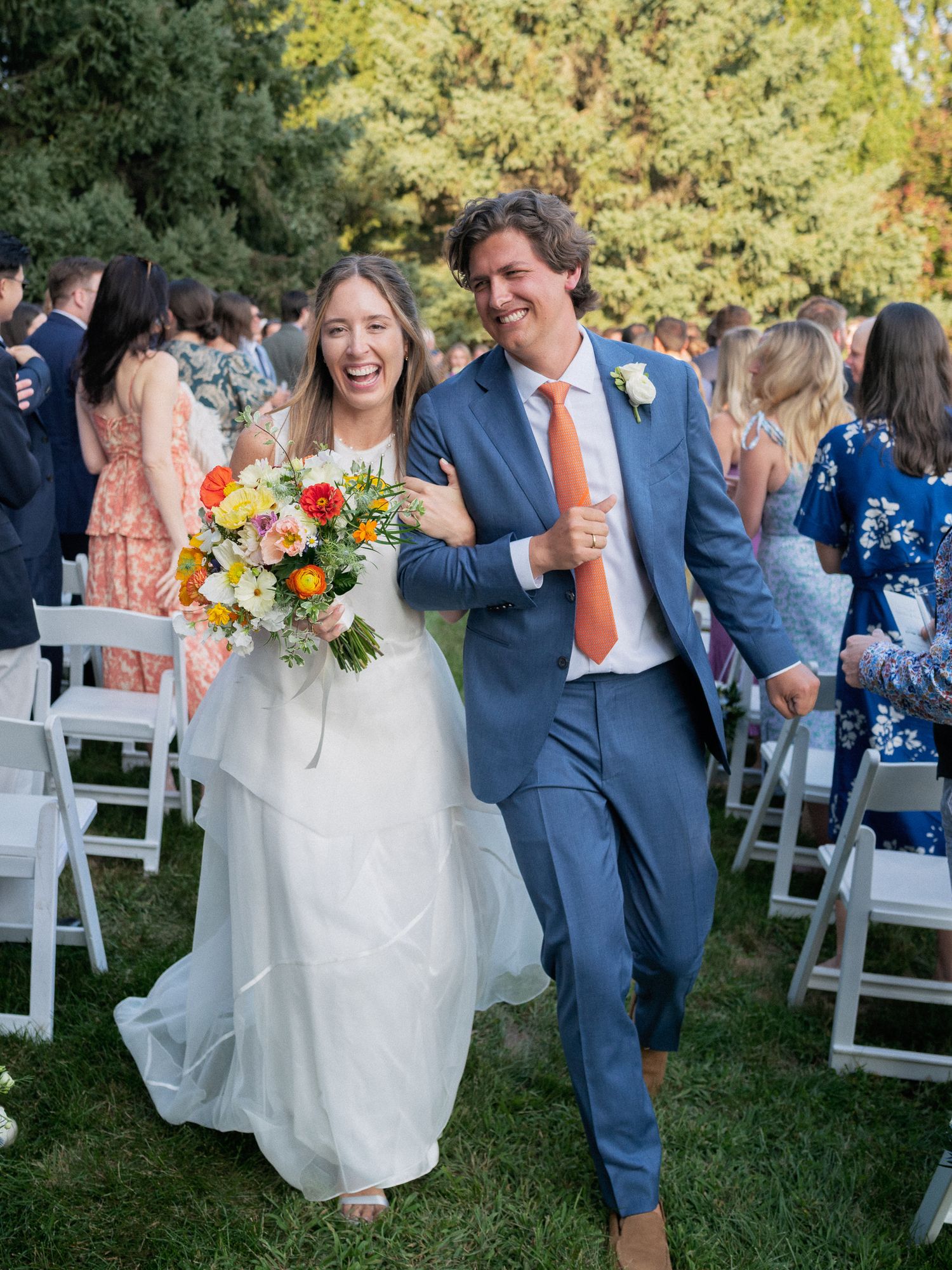 Joyful bride and groom walking down the aisle after wedding ceremony on a sunny outdoor lawn.