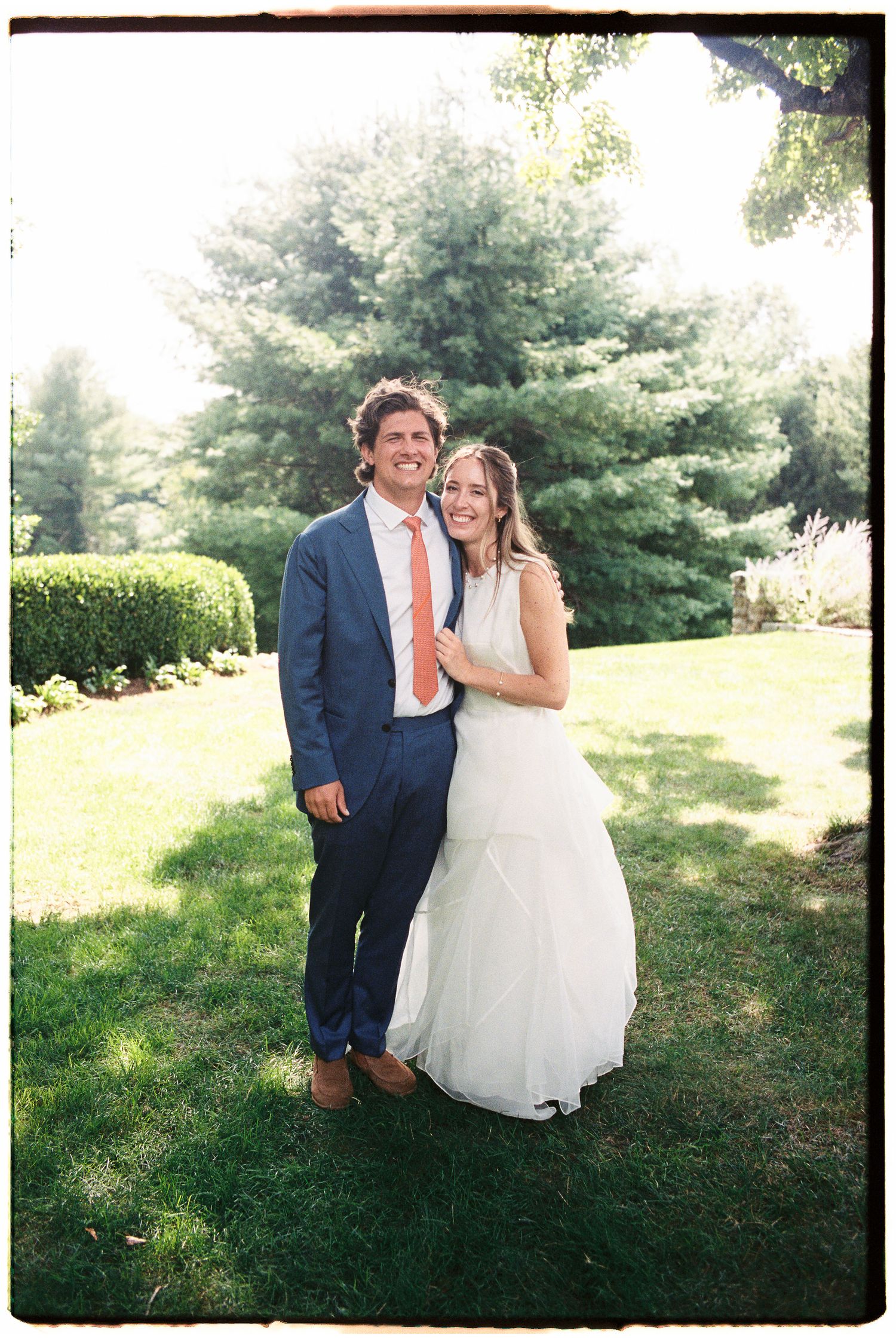 Smiling bride and groom posing together in a lush green garden on their wedding day.