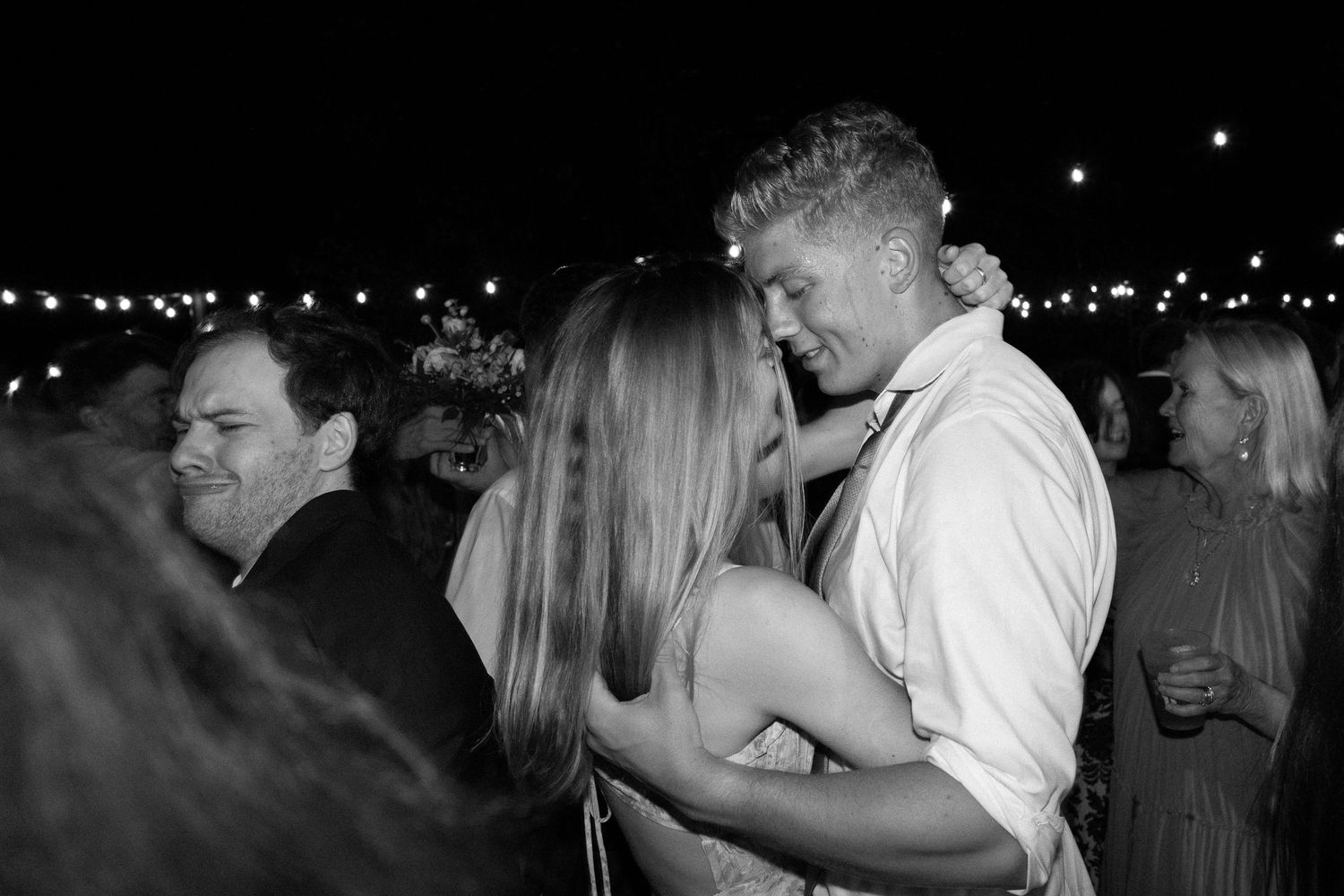 Black and white photo of couple sharing a romantic dance embrace at an evening wedding reception.