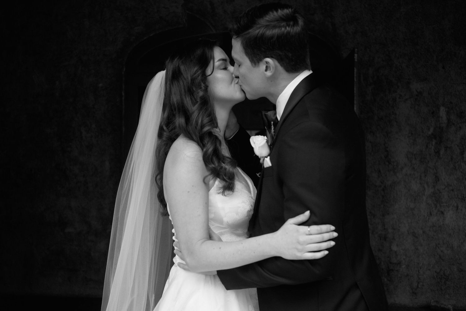 Black and white photo of a bride and groom sharing their first kiss at the wedding.