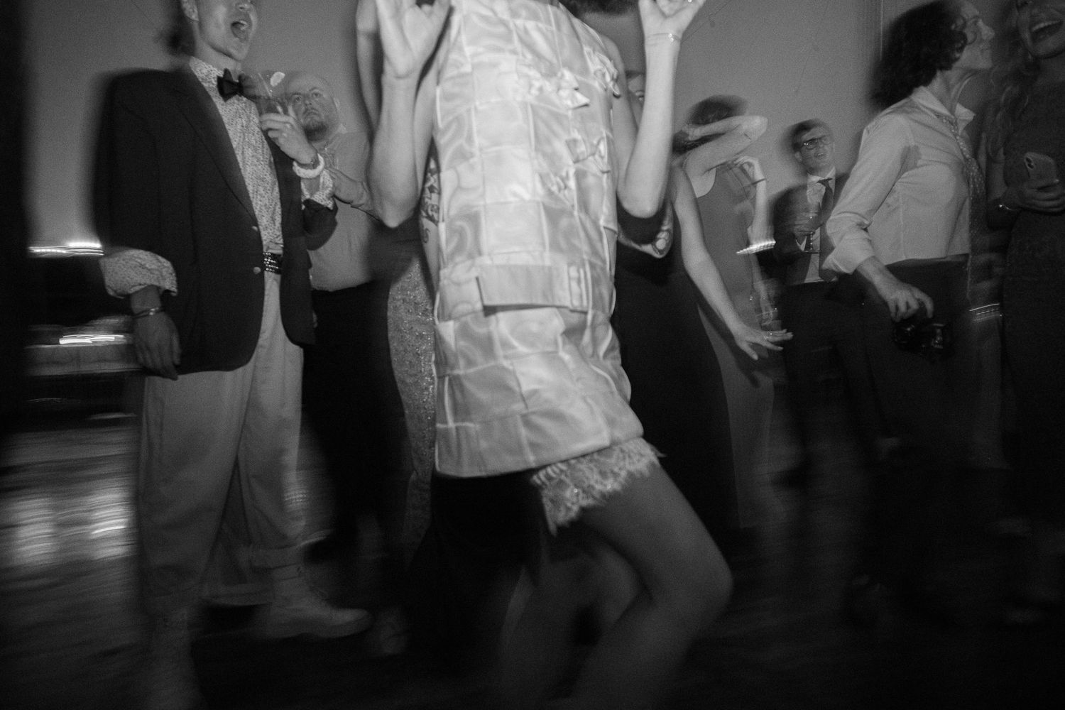 Black and white photo of guests dancing energetically on the floor at a wedding reception.