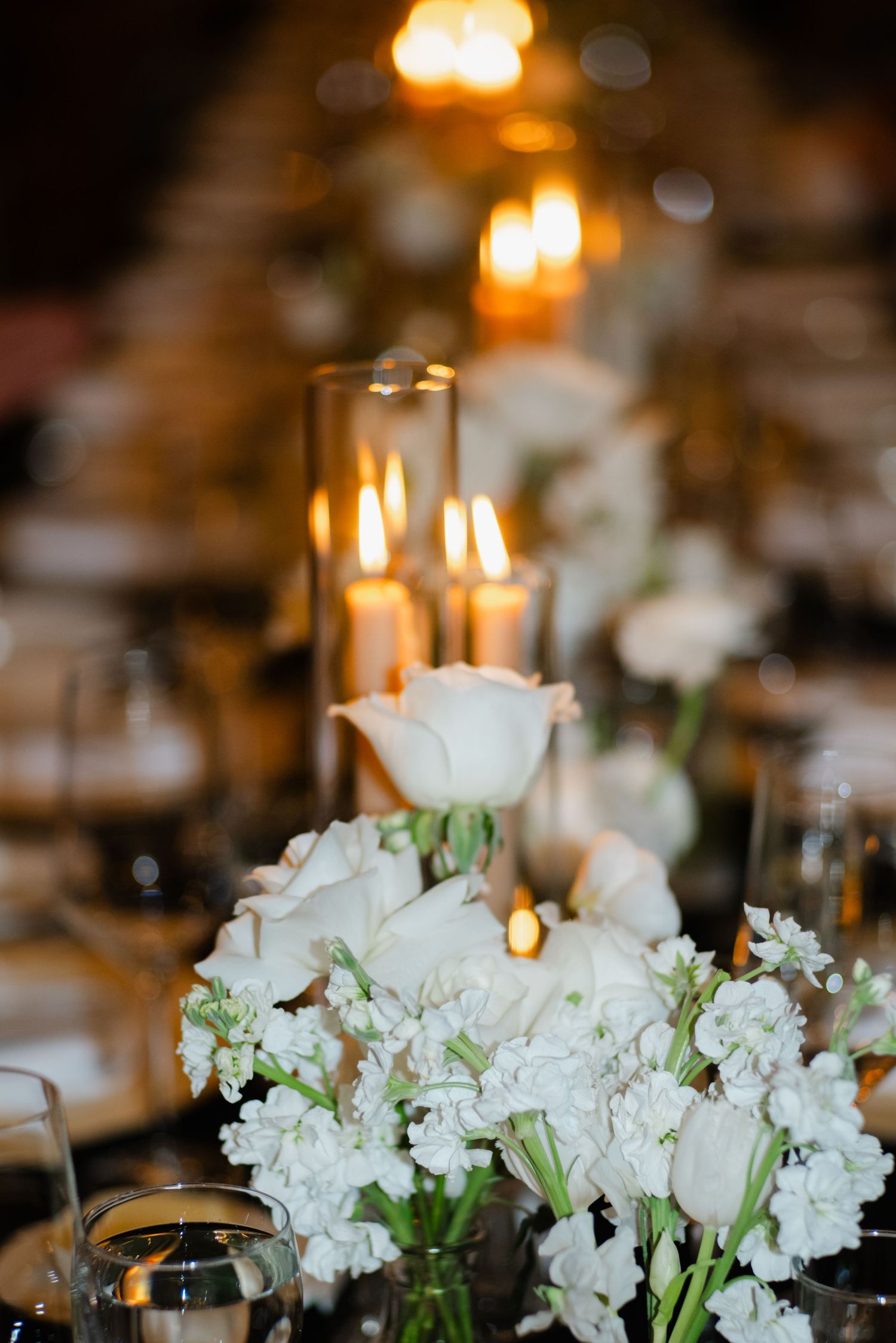 White roses and stock flowers with glowing pillar candles on wedding reception table.