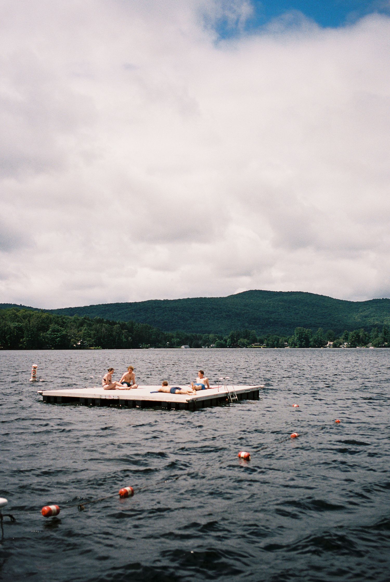 People relaxing on a floating dock platform in the middle of a calm mountain lake.