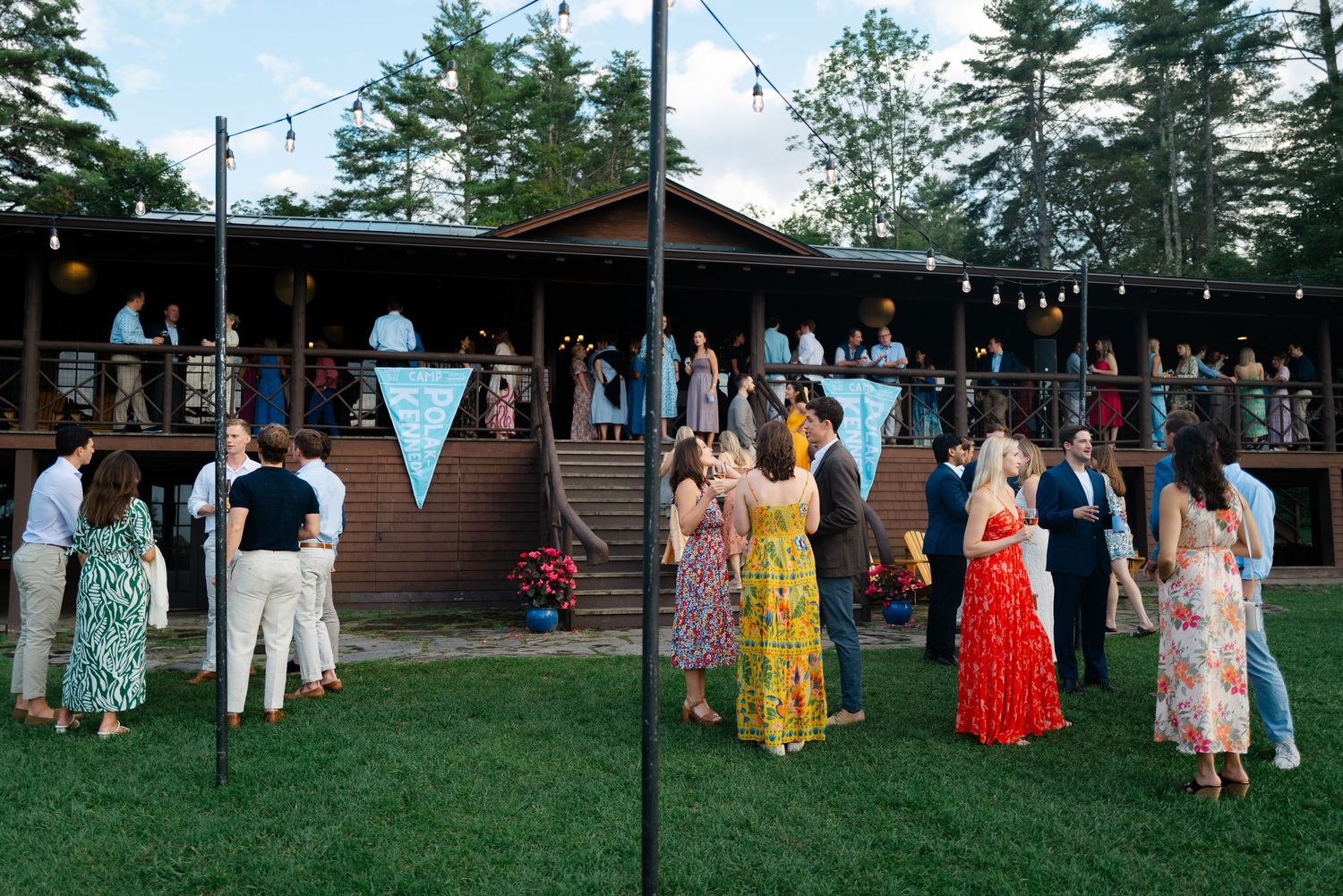 Guests mingle on the lawn and deck of a rustic lodge during an outdoor evening wedding reception.