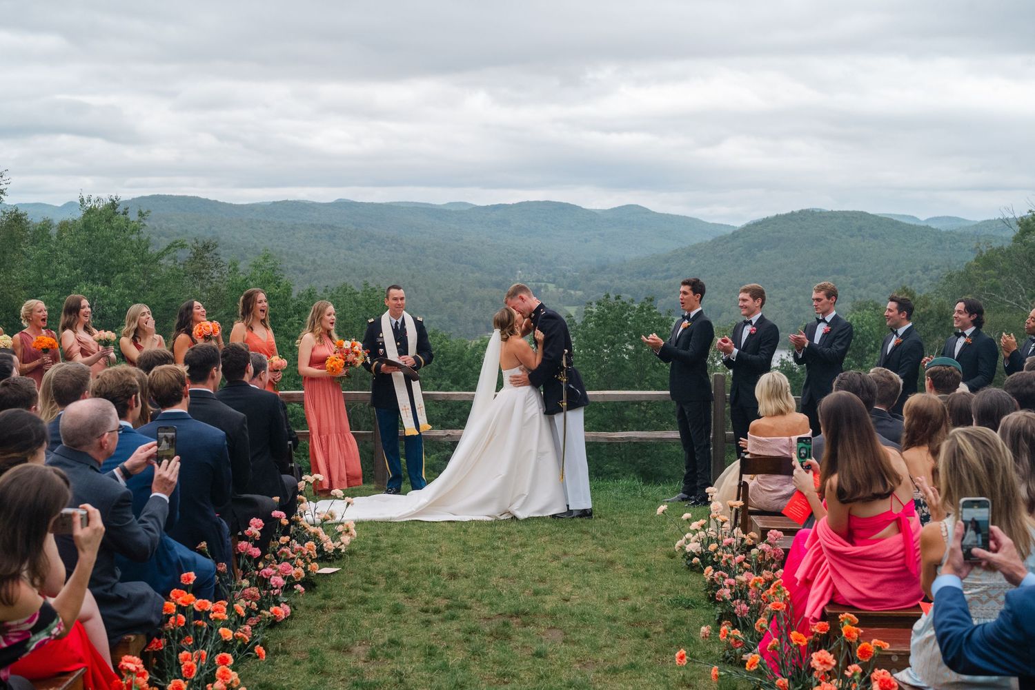 Outdoor wedding ceremony with bride and groom kissing at the altar, bridal party, and mountain views.