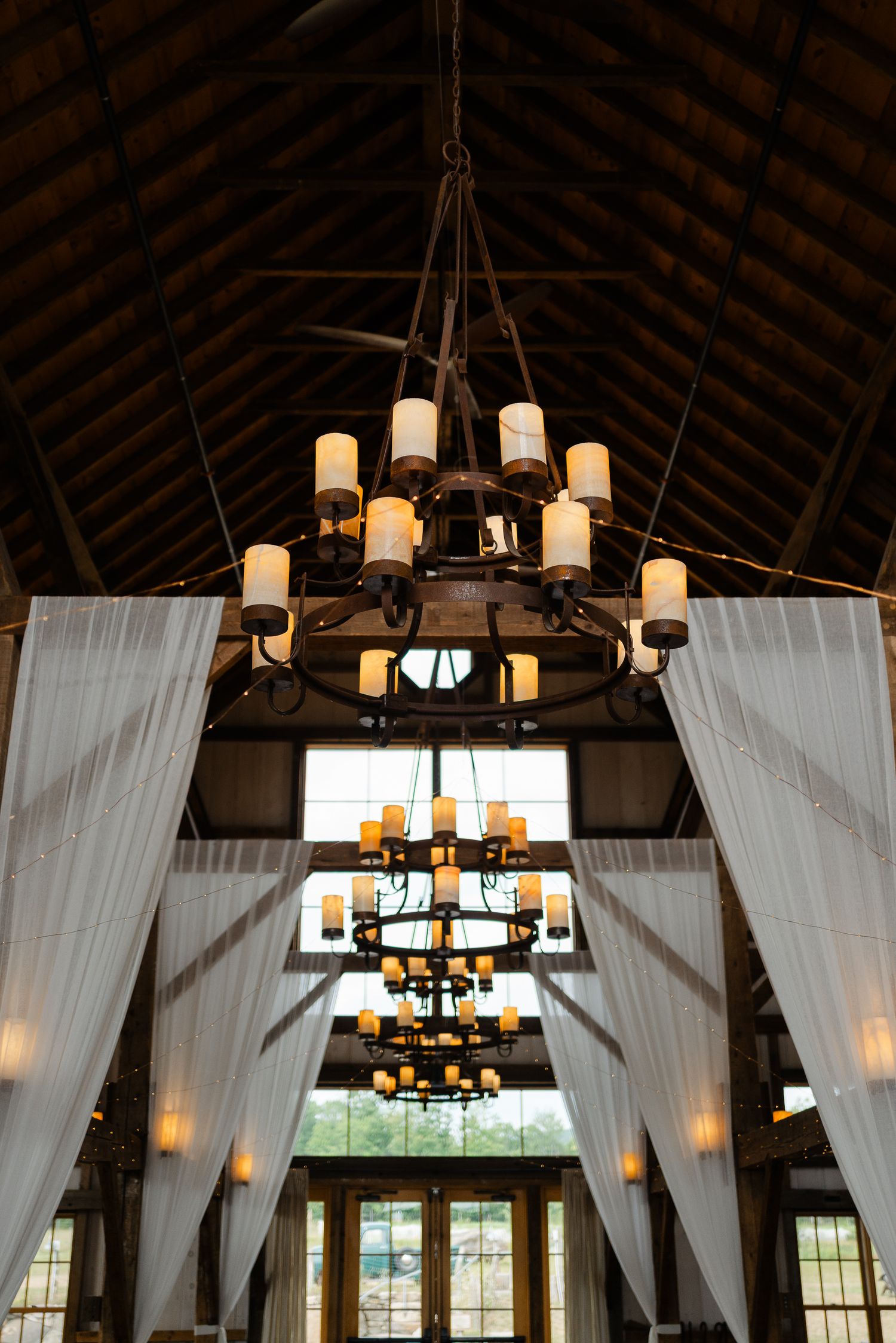 Rustic barn wedding venue with grand chandeliers and white draping decor.