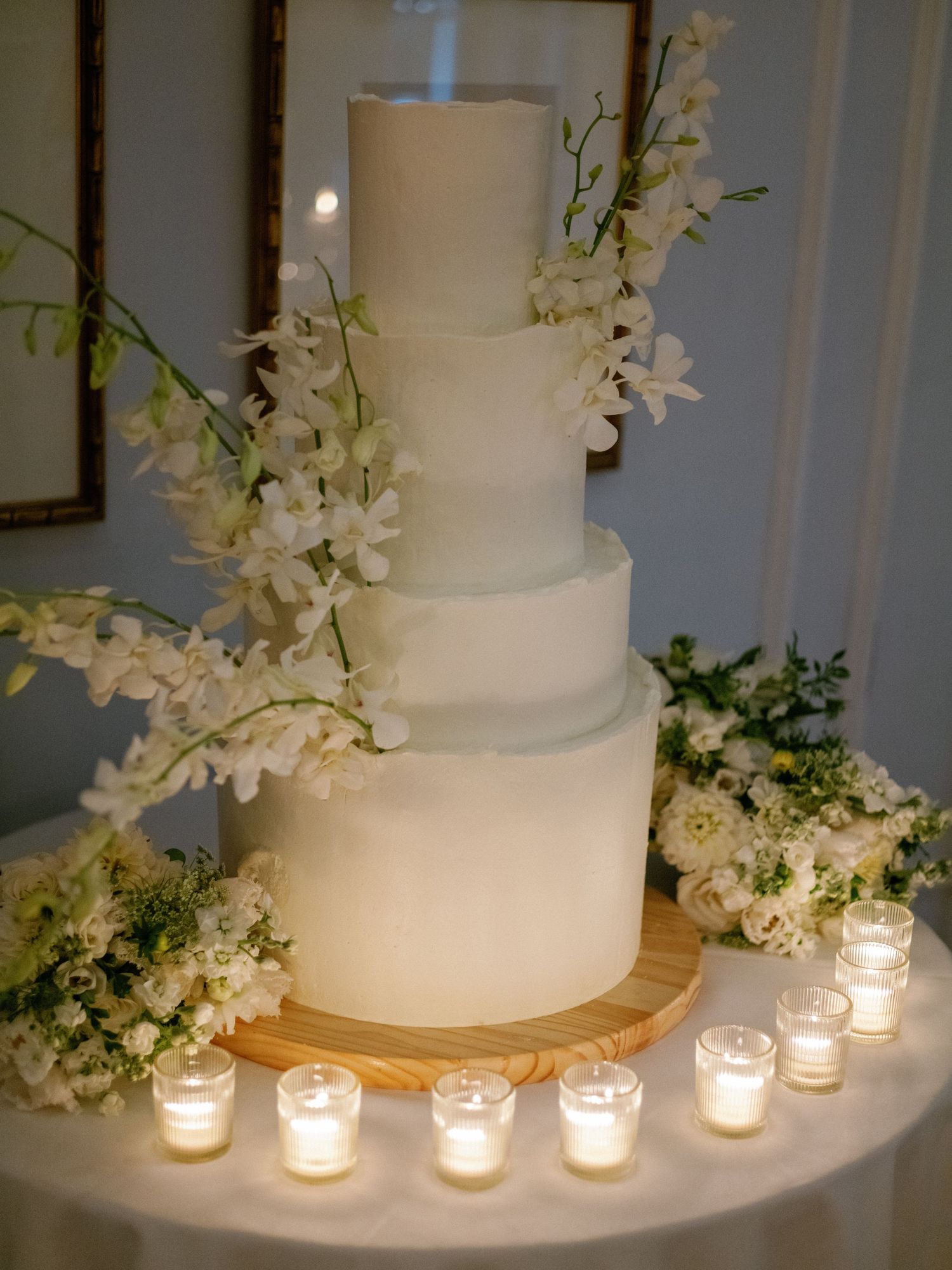 Elegant four-tier white wedding cake adorned with white orchids and surrounded by votive candles.