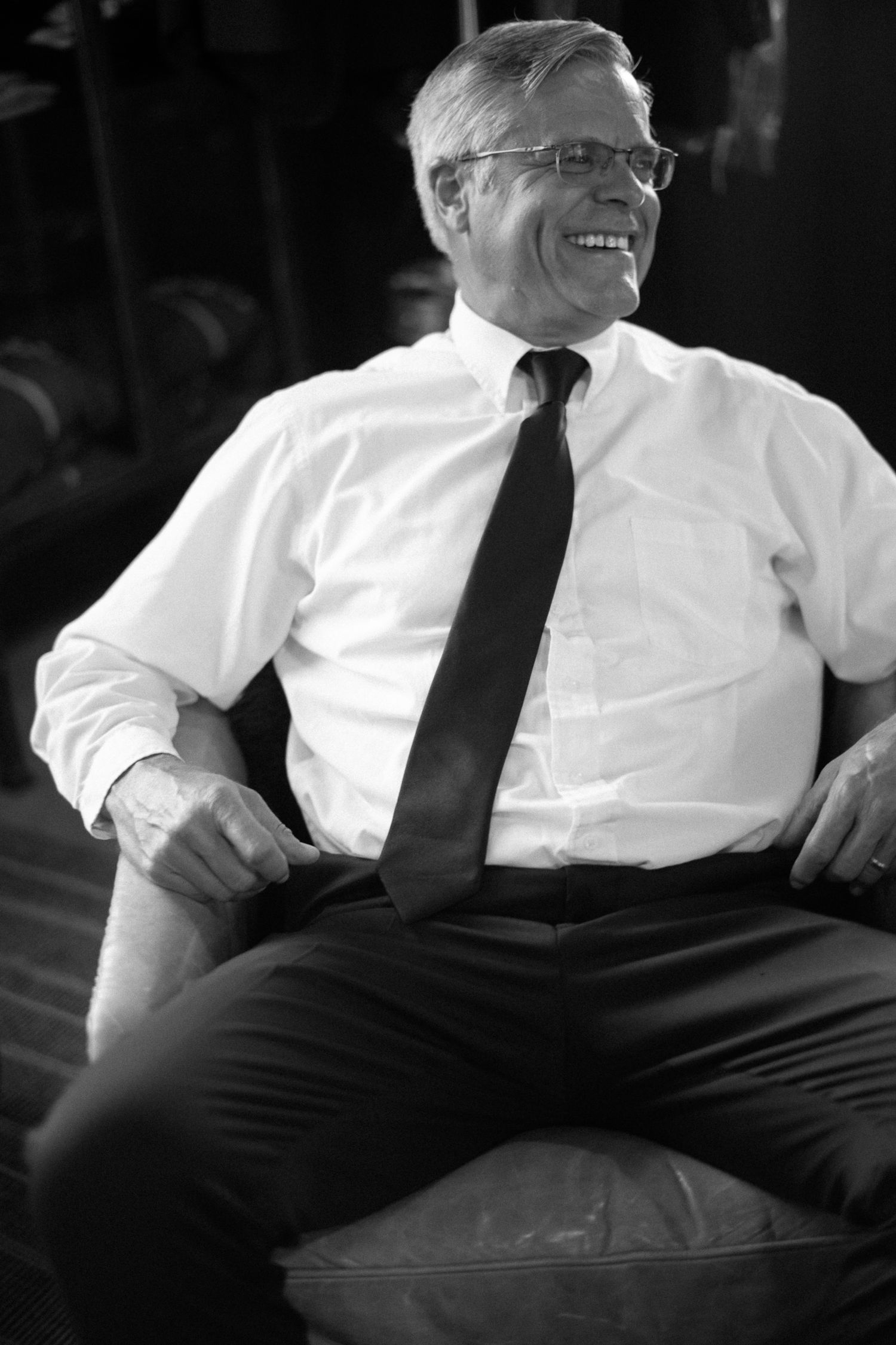 Black and white photo of smiling older man in white shirt and tie.